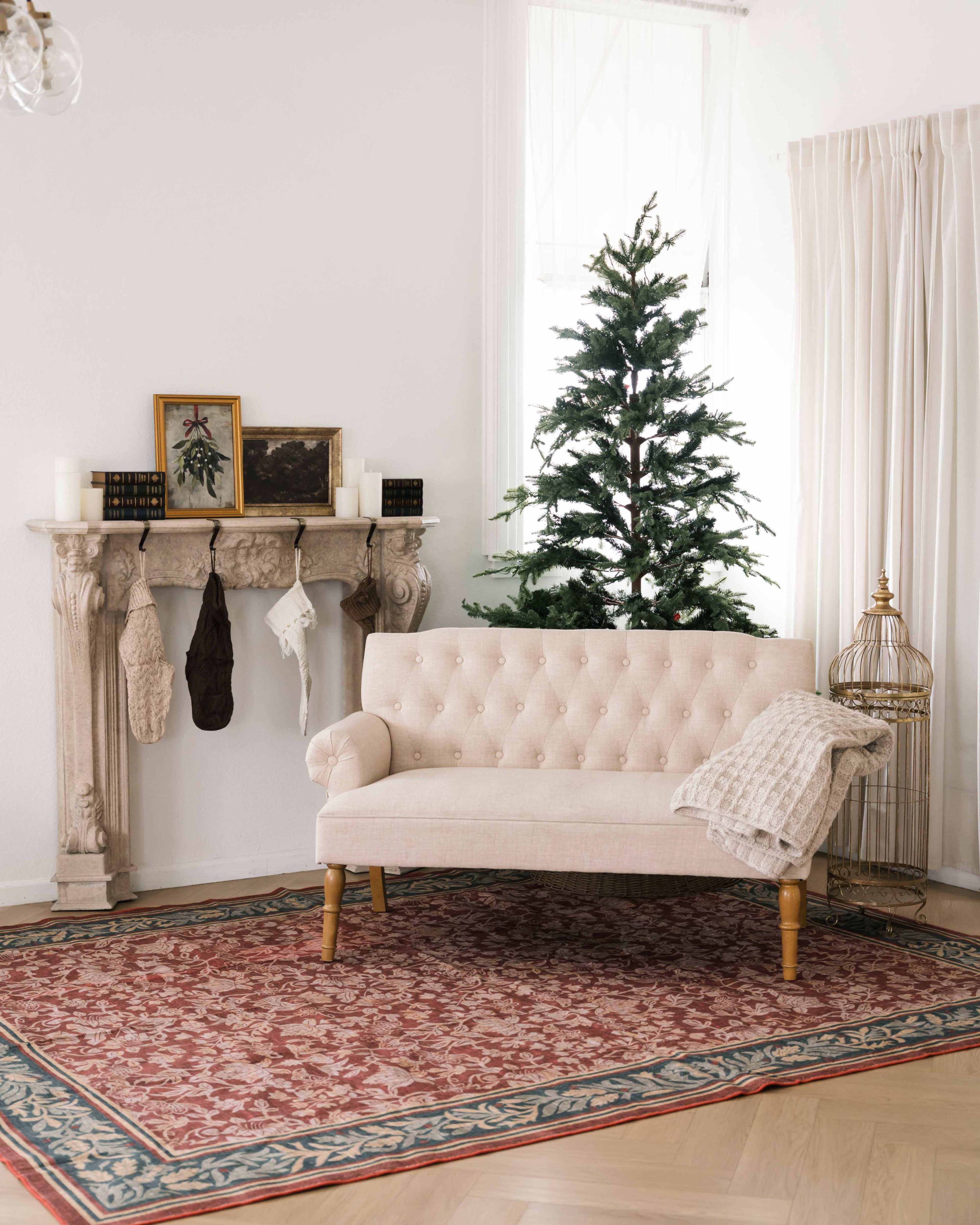 The image features a cozy living room setting with a tufted beige loveseat, a decorative fireplace mantel, and a small Christmas tree.