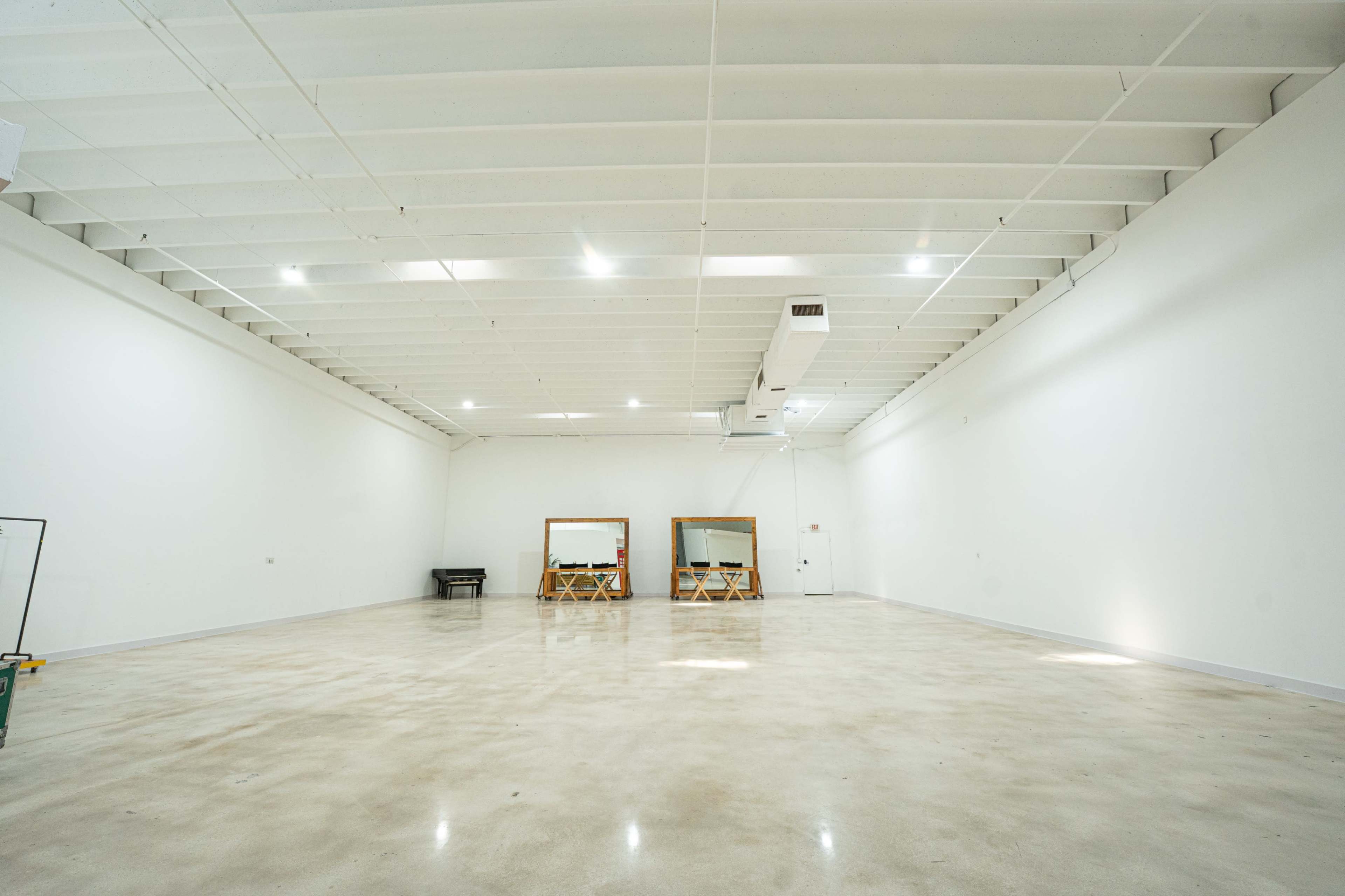 The image shows a large, empty room with white walls, a polished concrete floor, and two mirrors with wooden frames on the far wall.