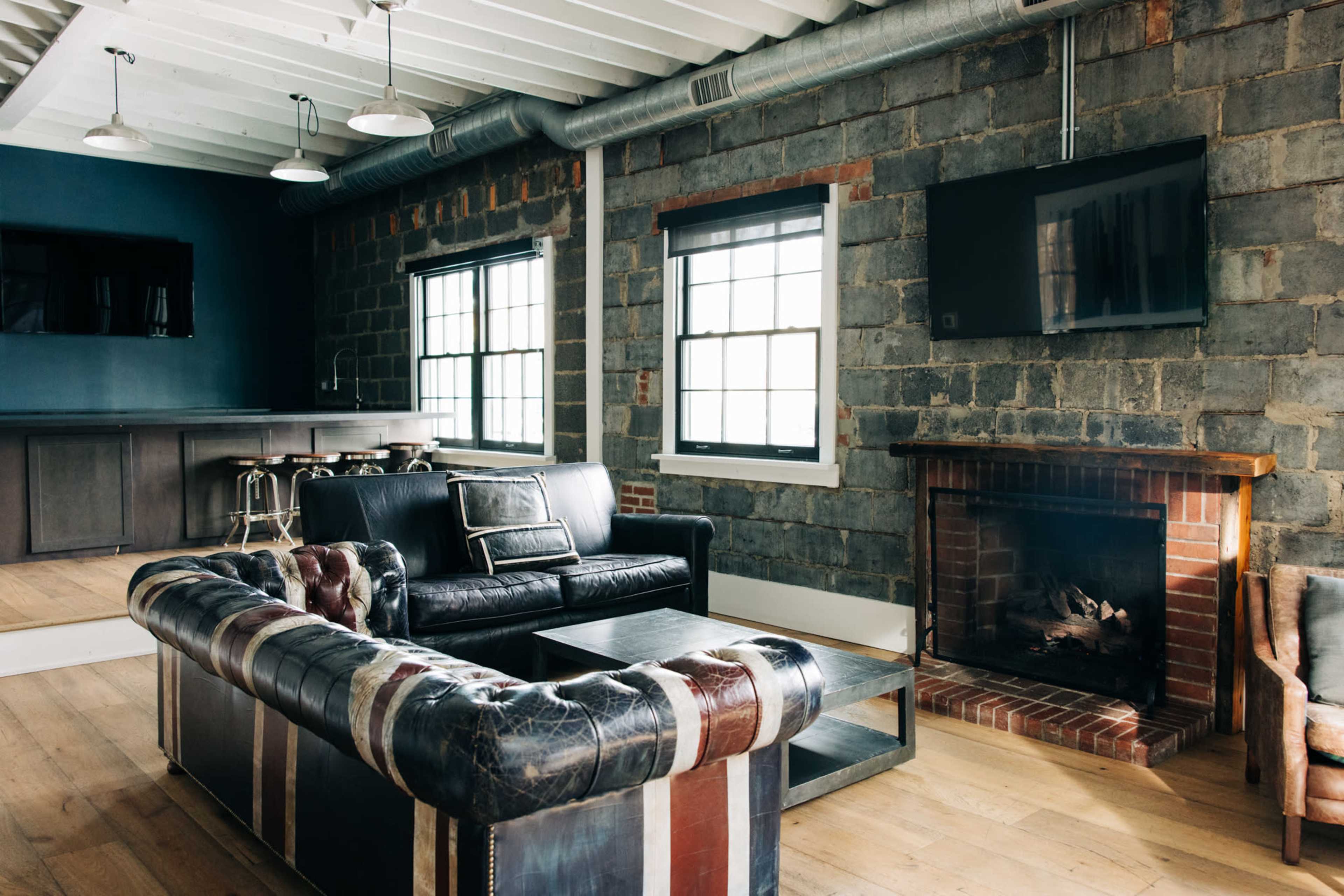 The image depicts a living room with a brick wall, a leather sofa, a coffee table, a fireplace, and a bar area in the background.