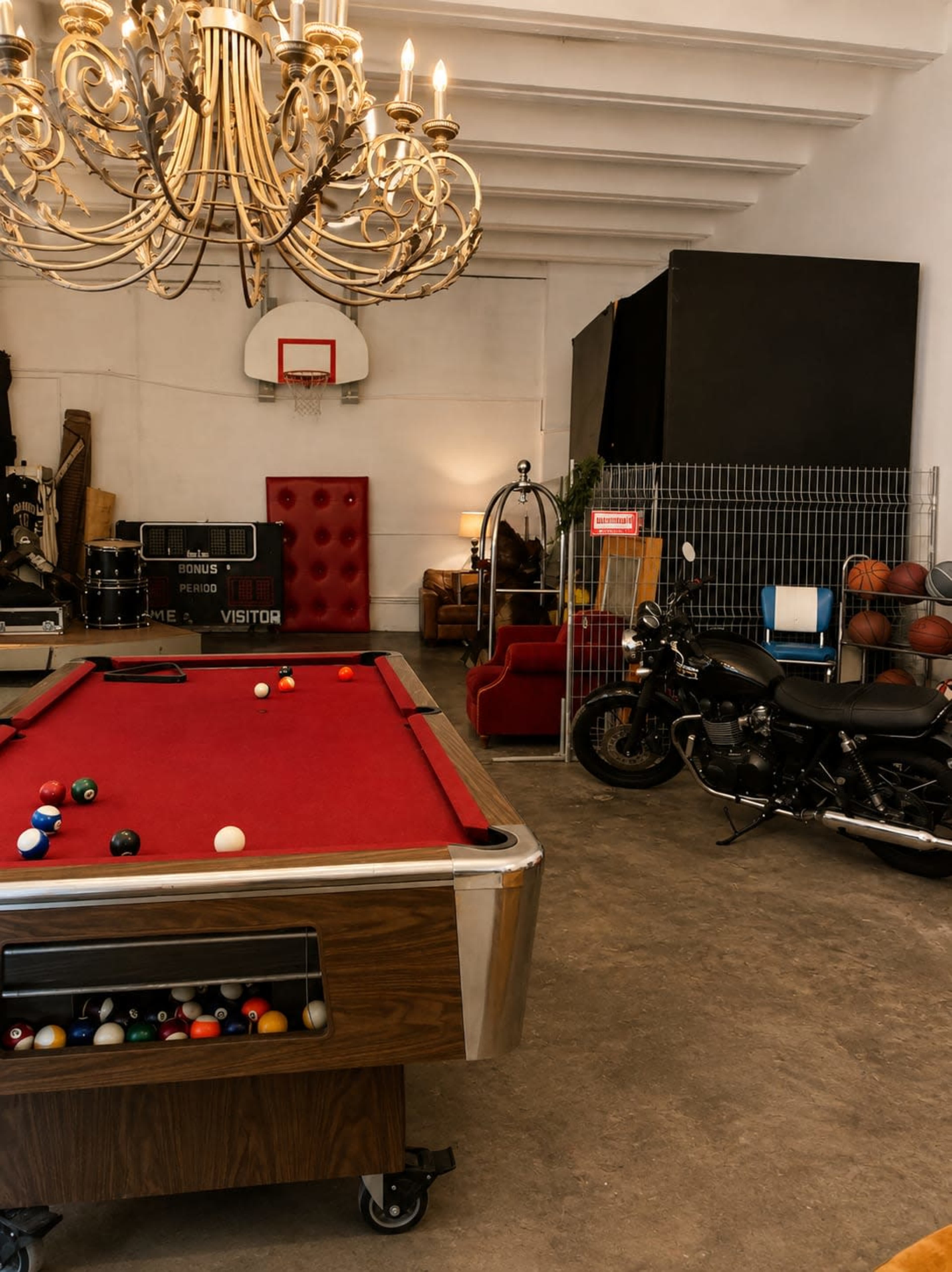 The image shows a games room featuring a red billiard table, a motorcycle, a basketball hoop, and various seating areas.