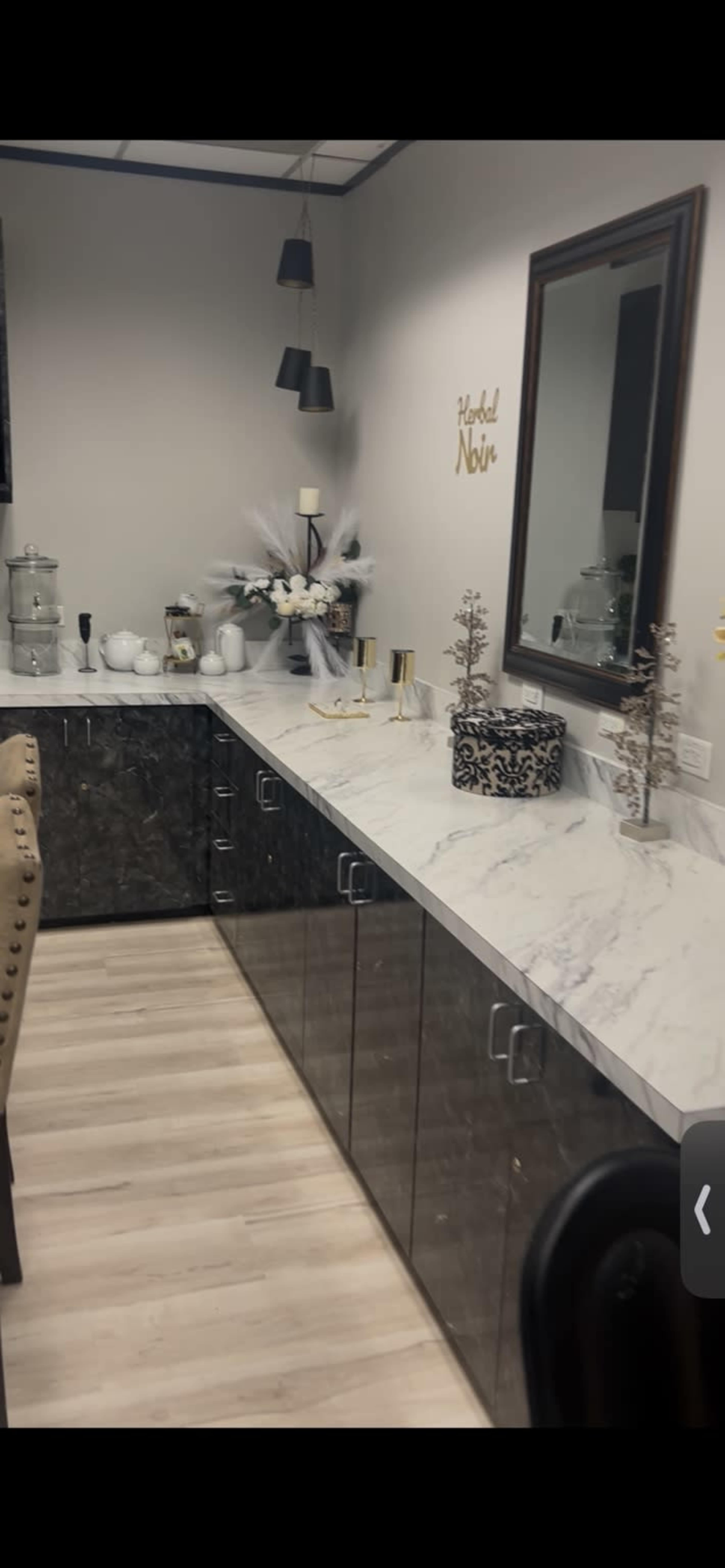 The image shows a modern interior space featuring a long counter with a marble top, cabinets below, decorative items, a large mirror on the wall, and subtle lighting.