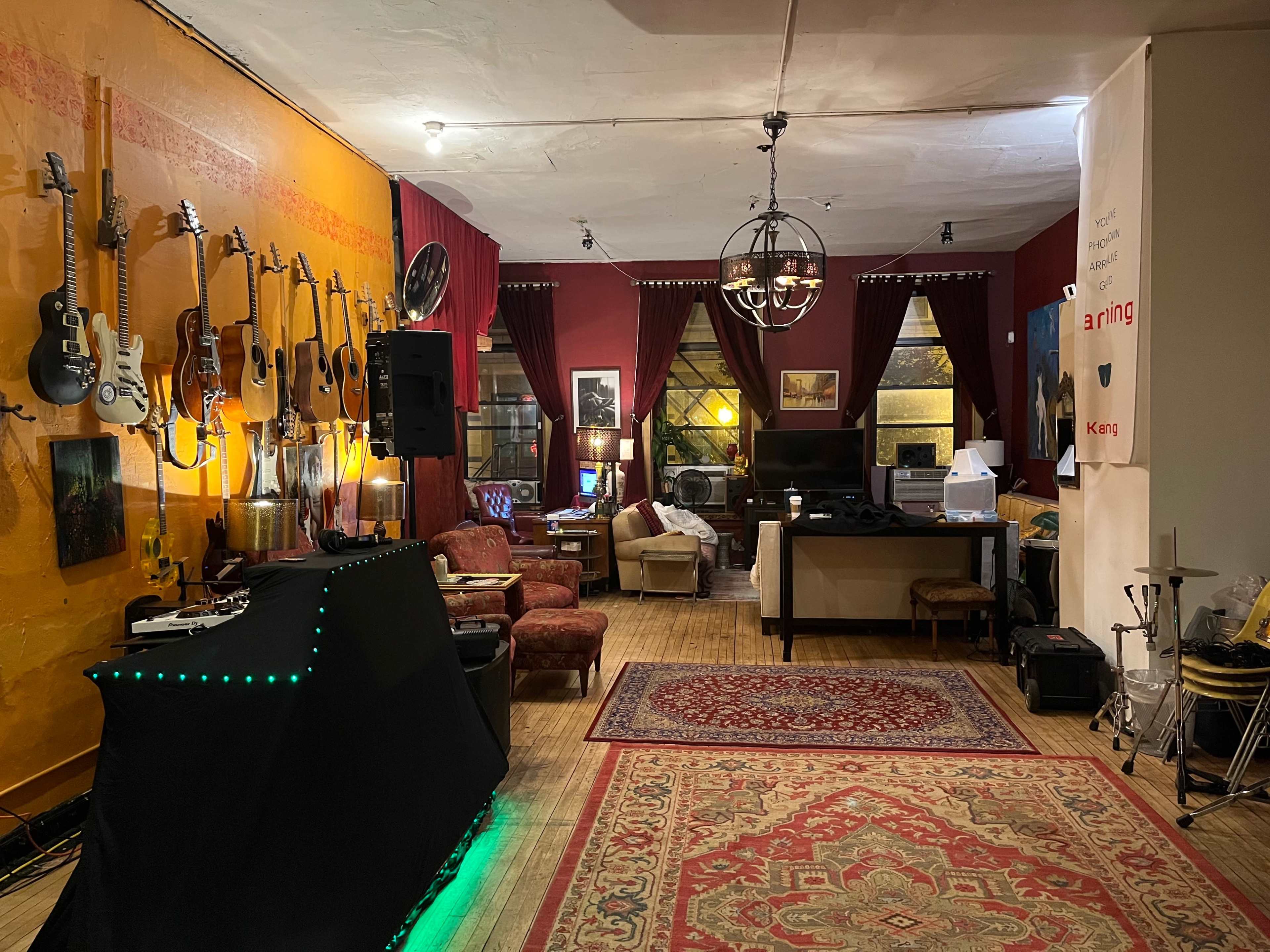 A cozy room with various guitars hanging on the wall, a sound system setup, and seating areas arranged around a central rug.