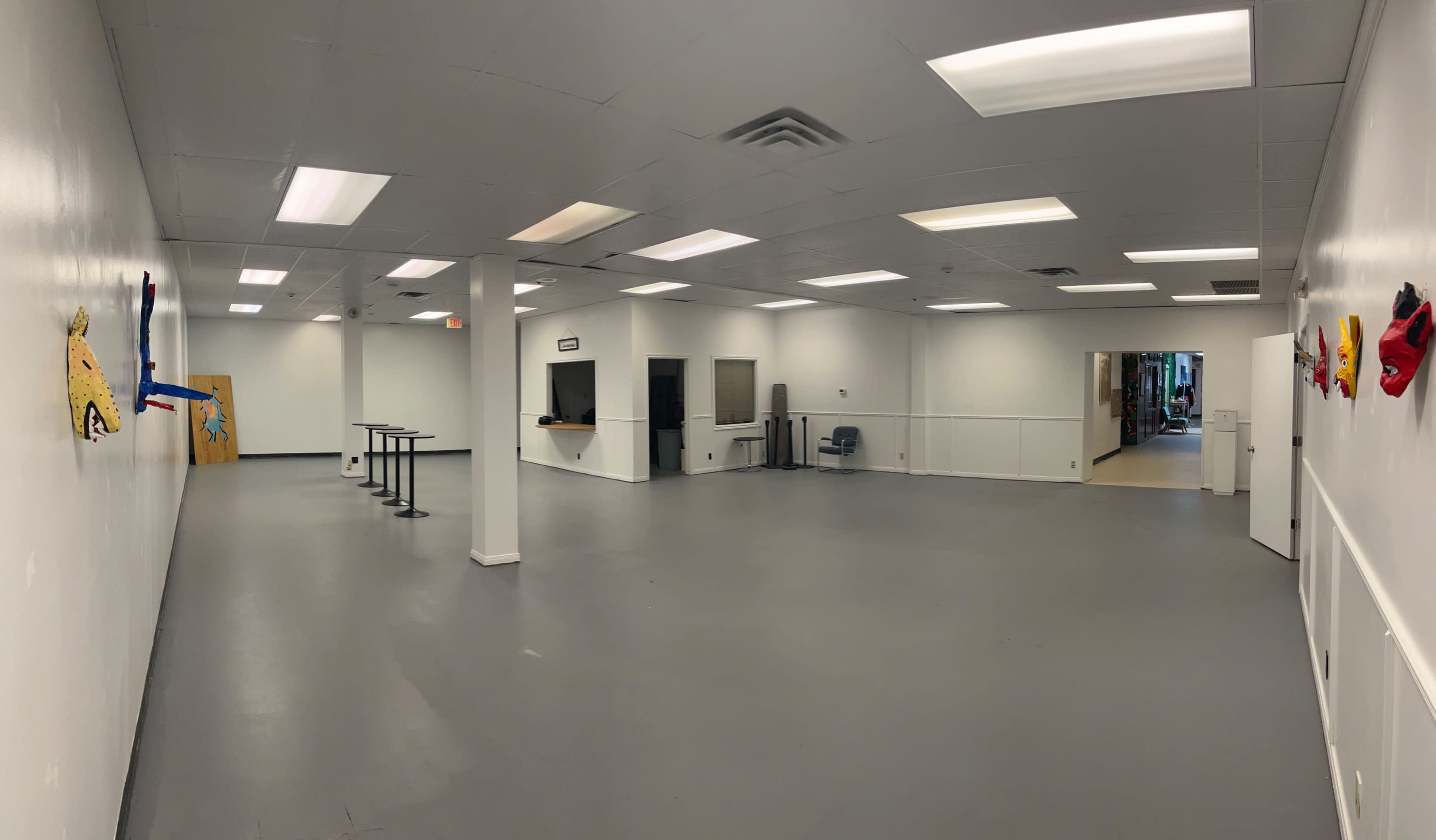 The image shows a spacious, empty room with gray flooring, white walls, and several overhead lights.