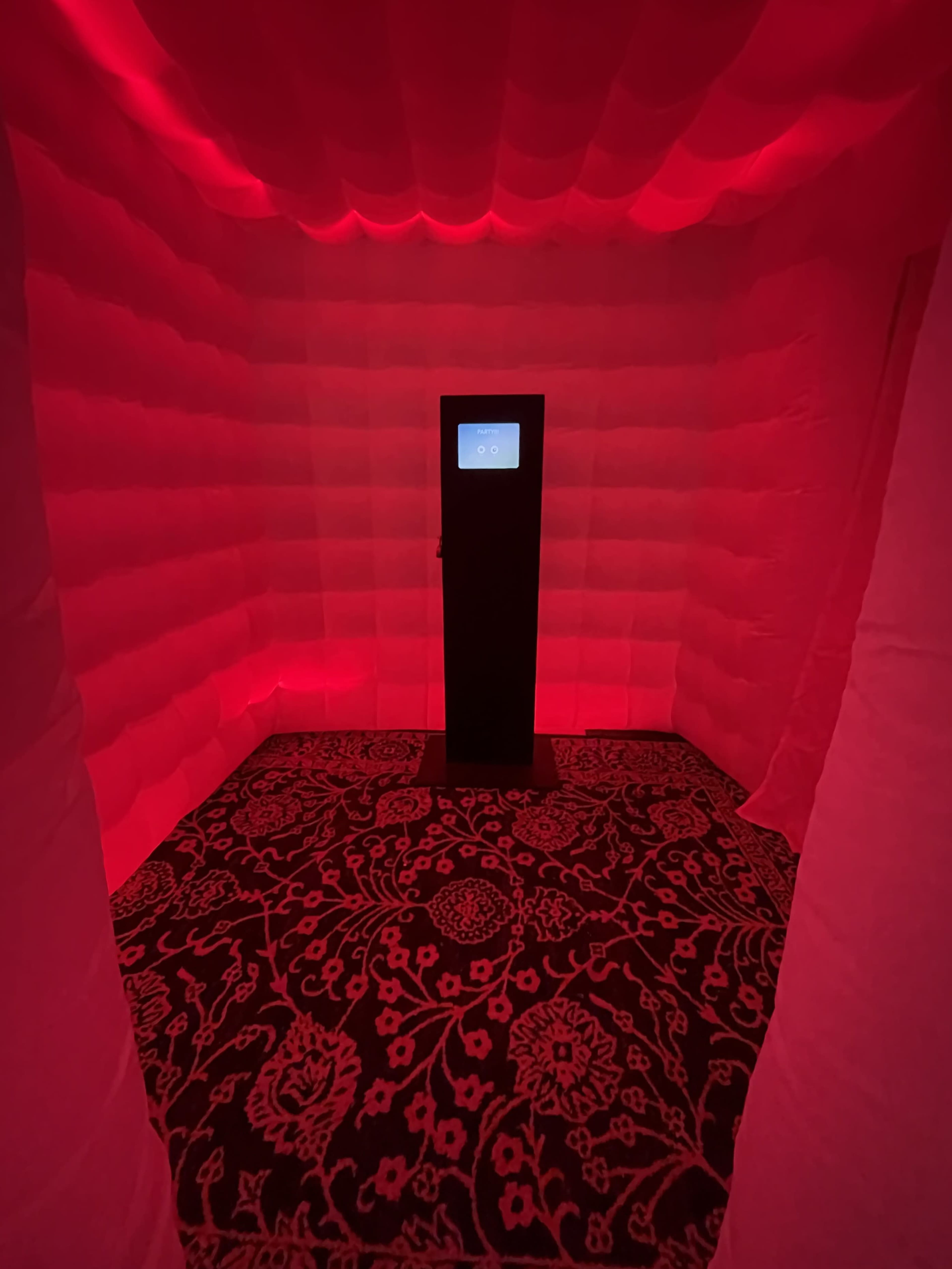 The image shows a small, enclosed room lit with red light, featuring a black display stand in the center.