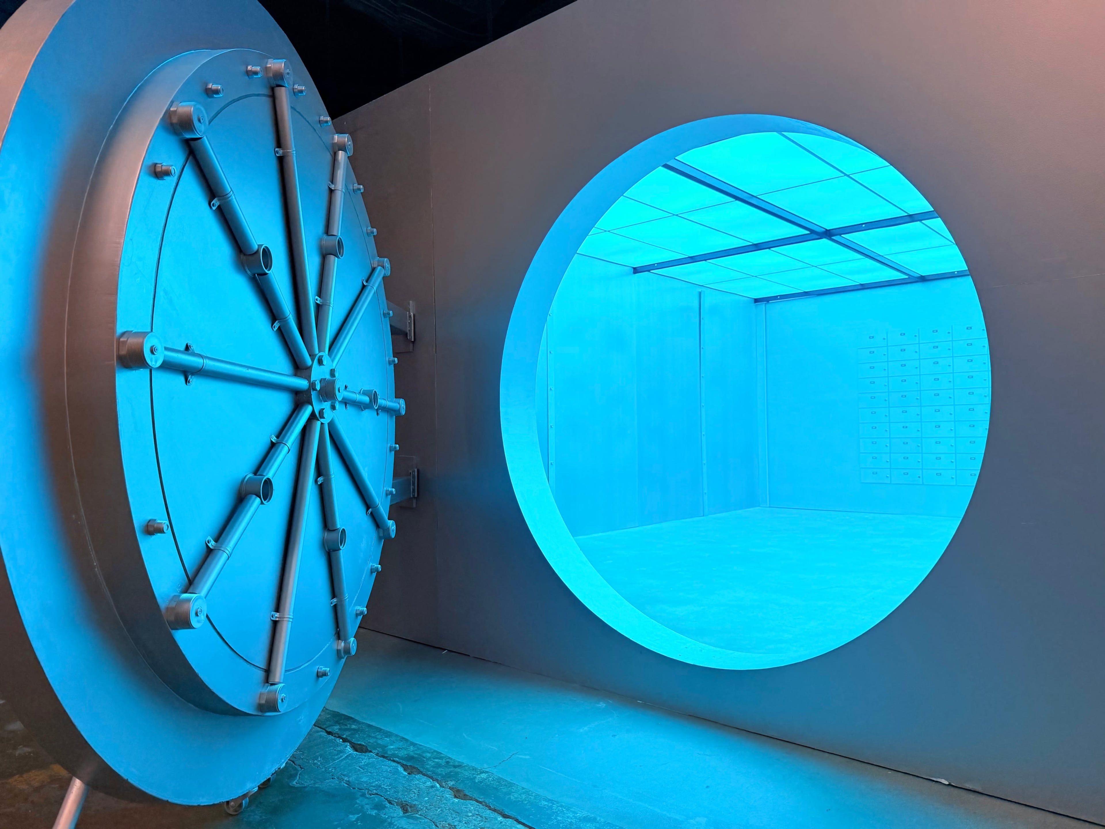 A large circular vault door stands open, revealing a brightly lit, blue-tinted interior space.