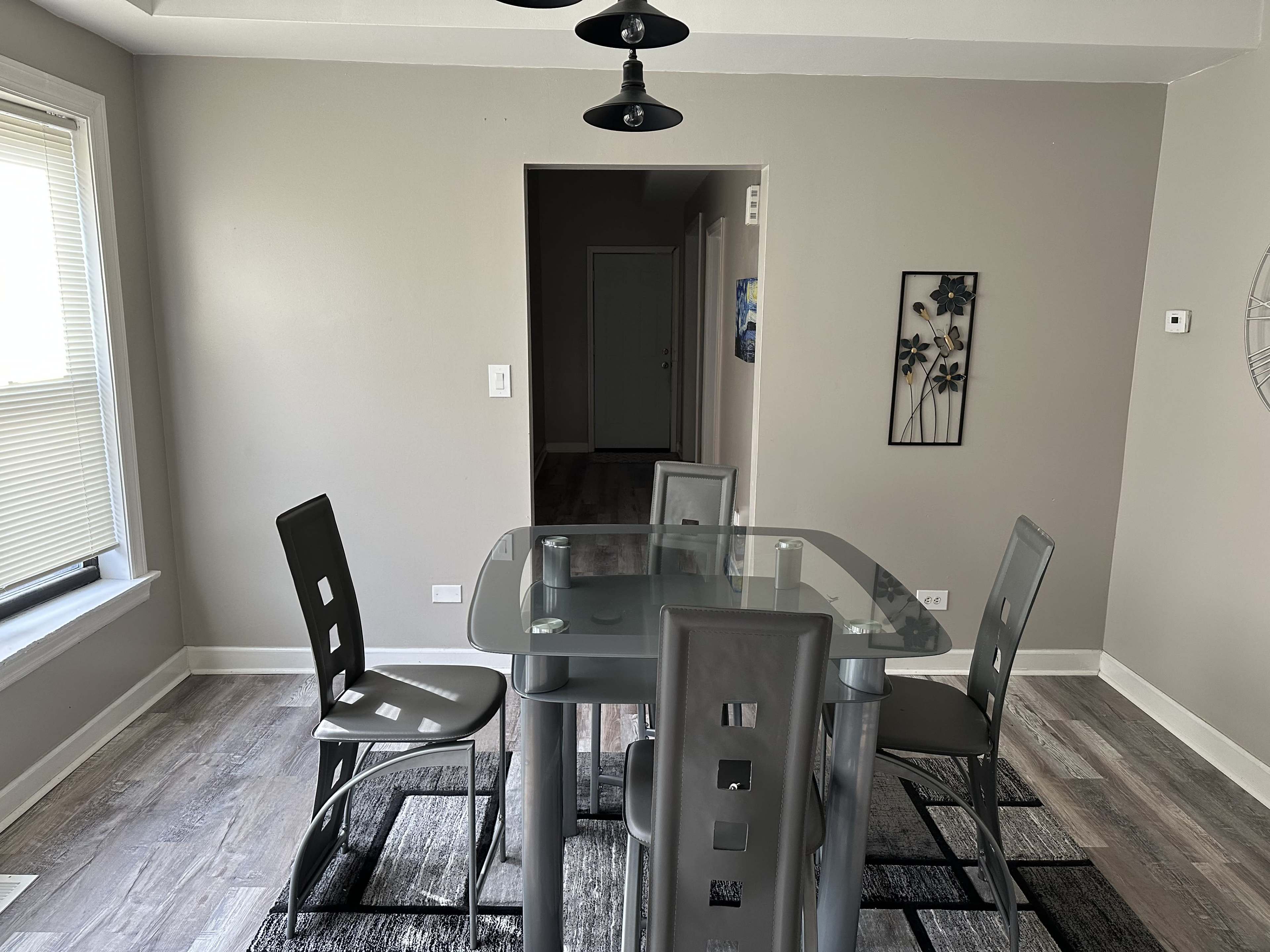 A modern dining area features a glass-top table surrounded by four chairs, with a light fixture hanging above.