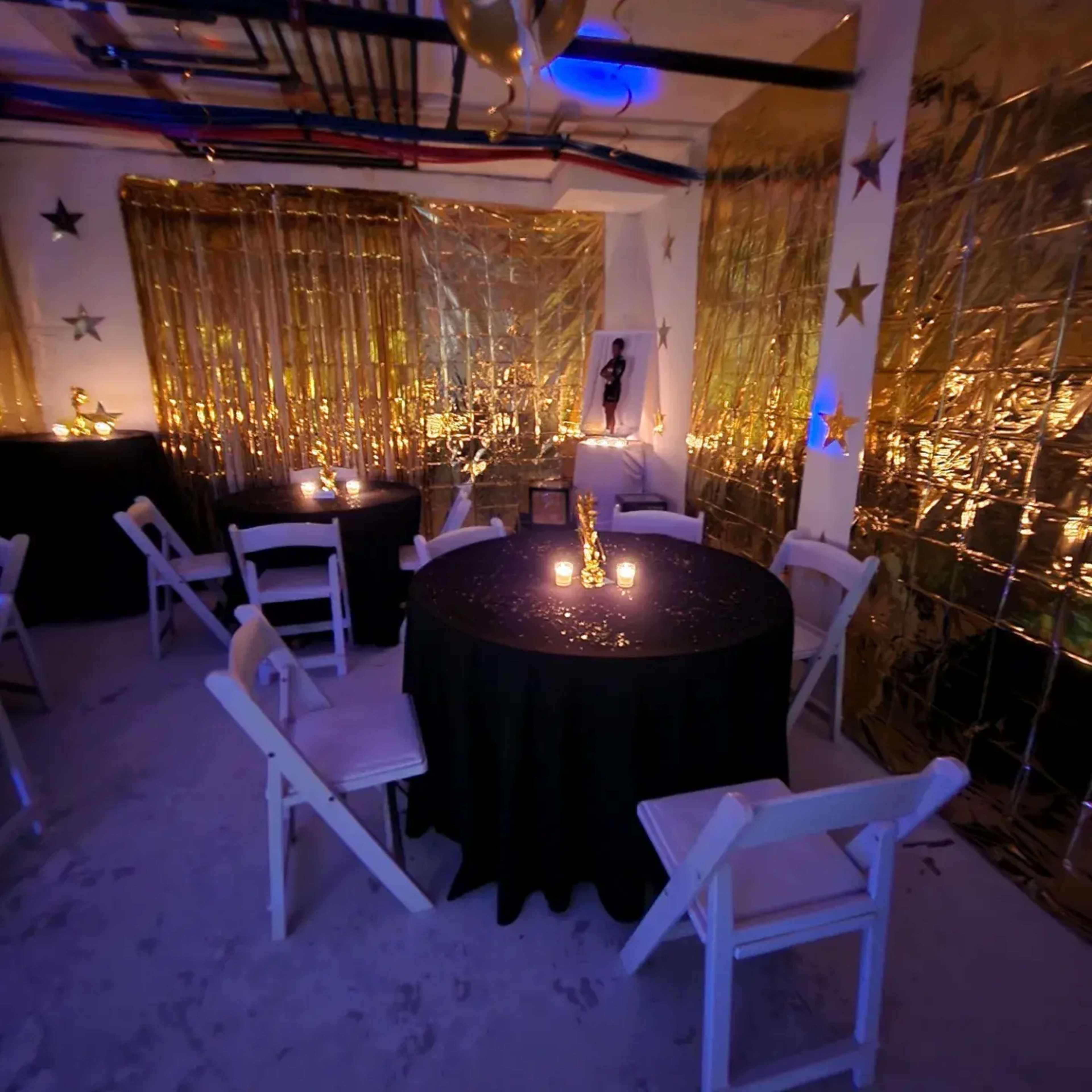 A decorated indoor space with tables covered in black cloth, golden drapery, and dim lighting from candles.