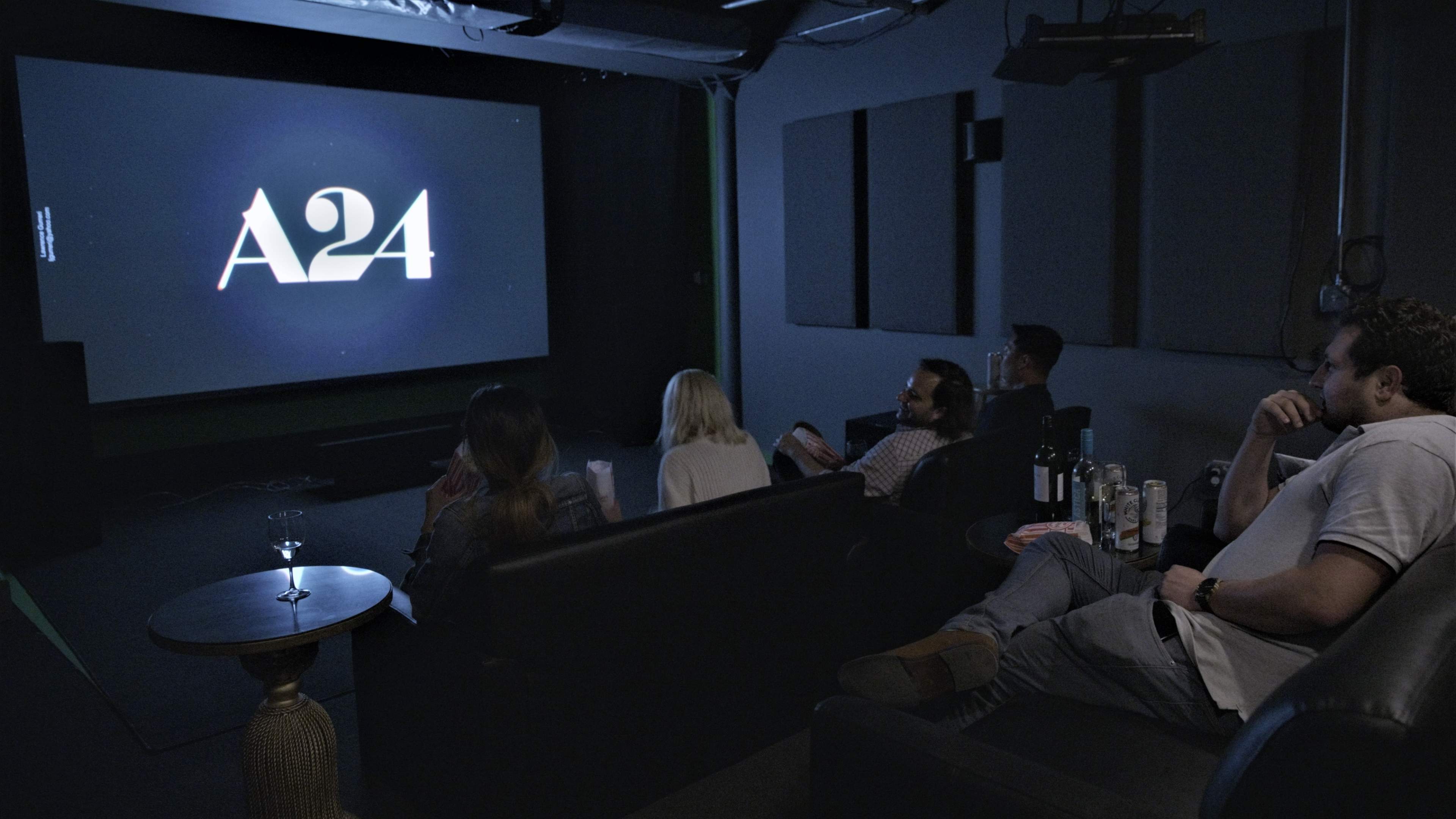 A group of five people watches a film on a large screen in a dimly lit home theater.