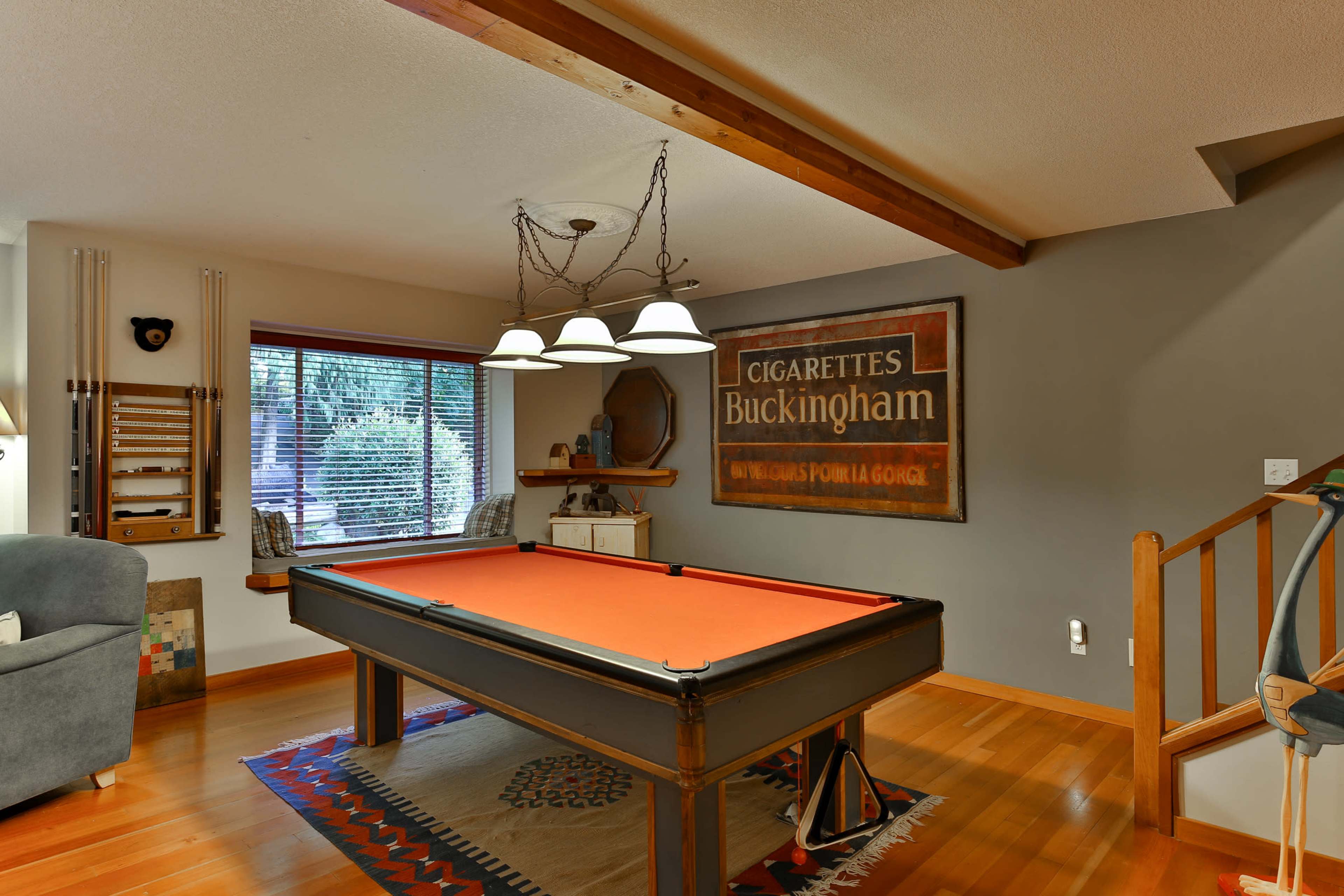 A billiard room with a black pool table, an orange felt surface, and a vintage sign on the wall, illuminated by a pendant light fixture.