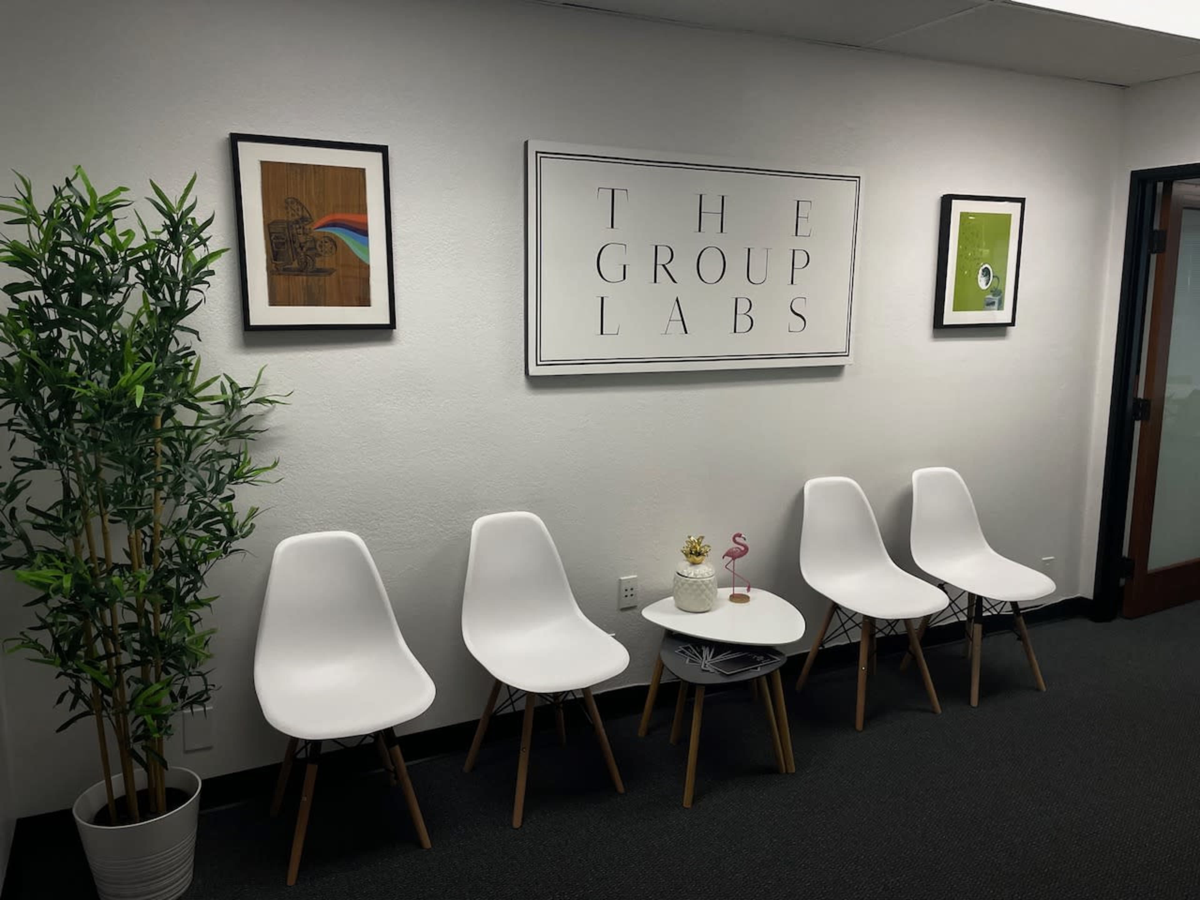 A waiting area with four white chairs, a potted plant, and framed artwork on the walls.