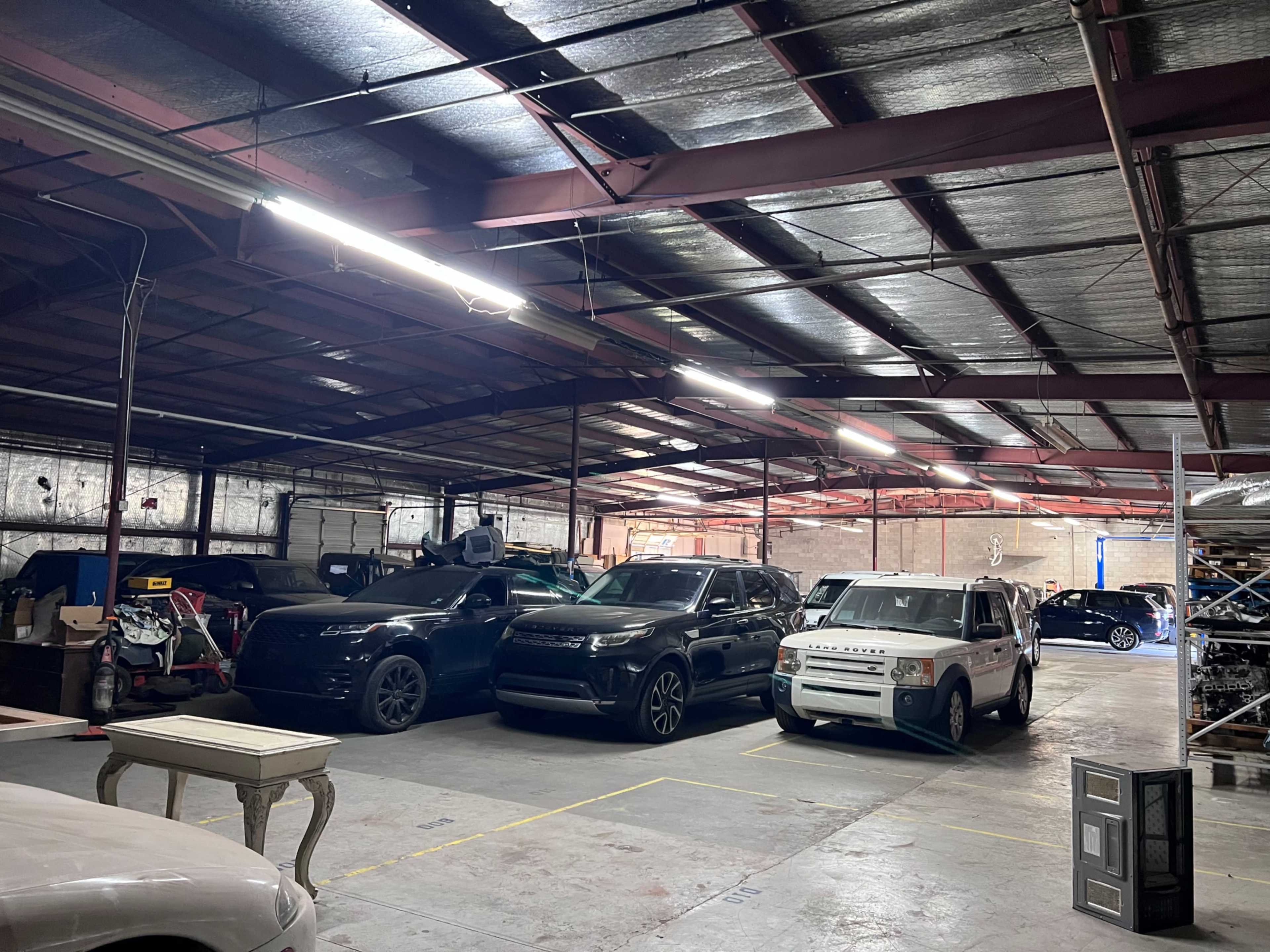 The image shows a spacious garage with several vehicles parked, including SUVs and a white car, all under fluorescent lighting.