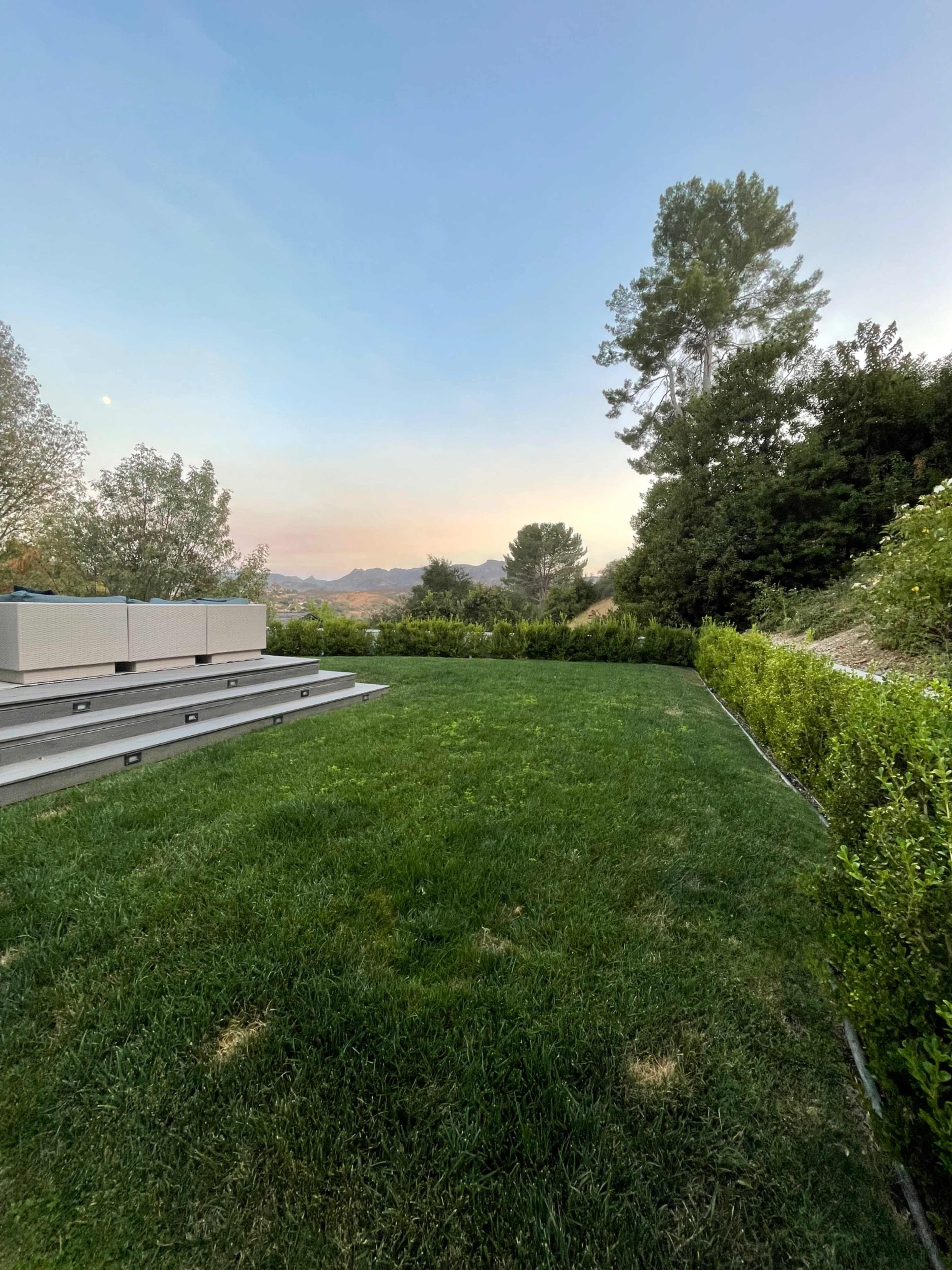 A green lawn with a wooden deck and trees in the background against a twilight sky.