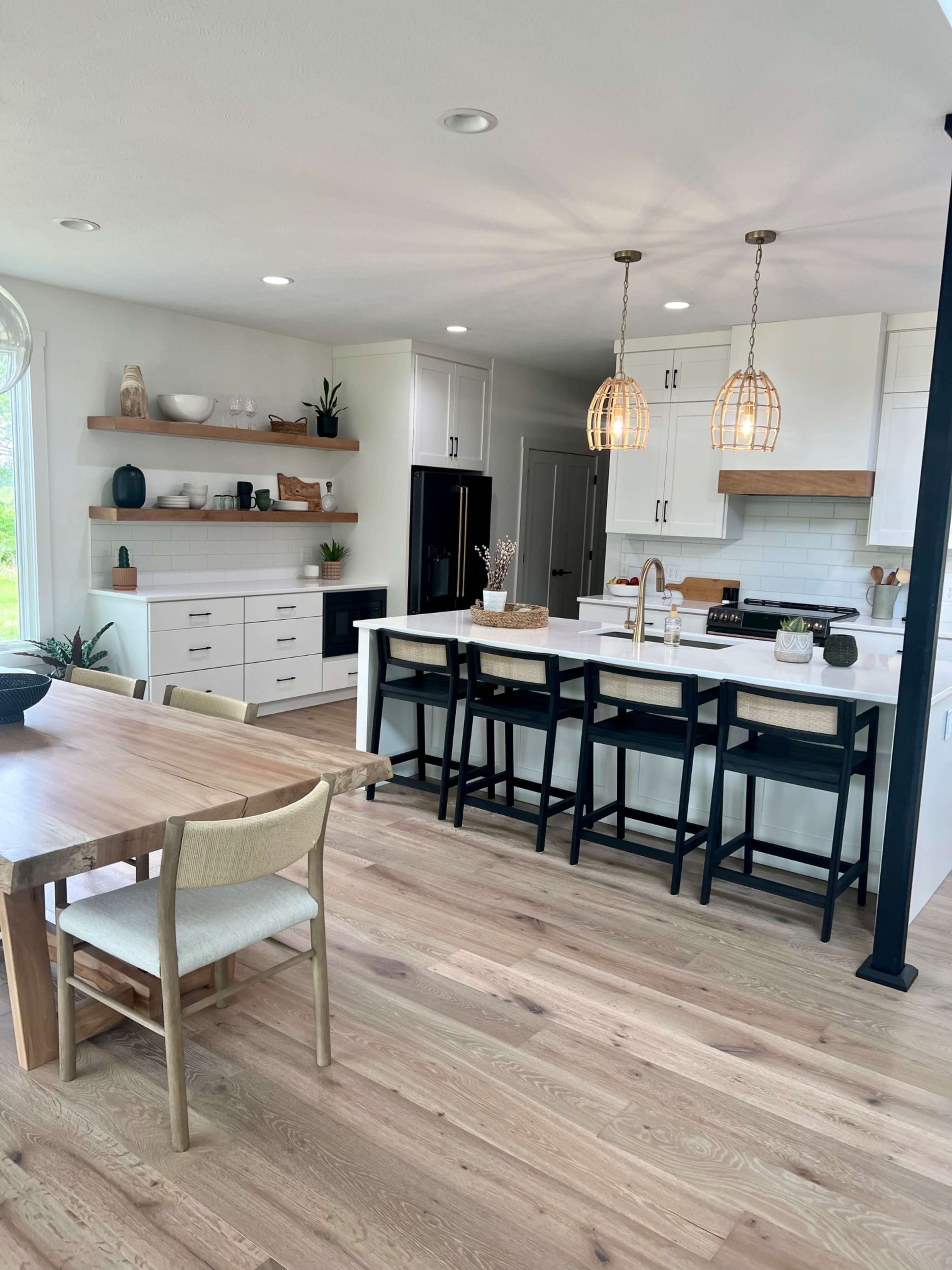 The image shows a modern kitchen featuring white cabinetry, a central island with bar seating, and a wooden dining table with chairs.