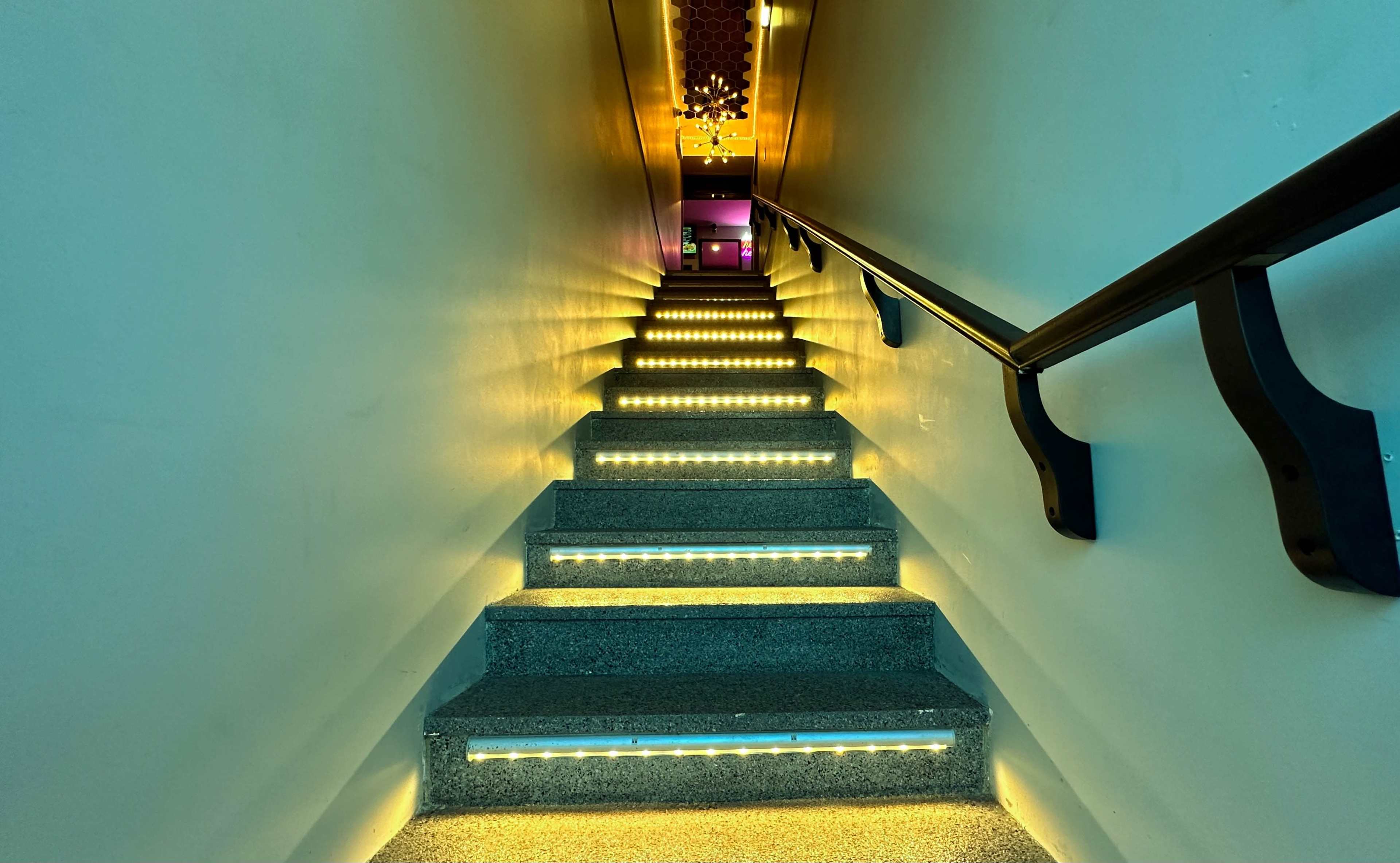 A staircase illuminated by LED lights along the steps, leading up to a brightly lit area at the top.