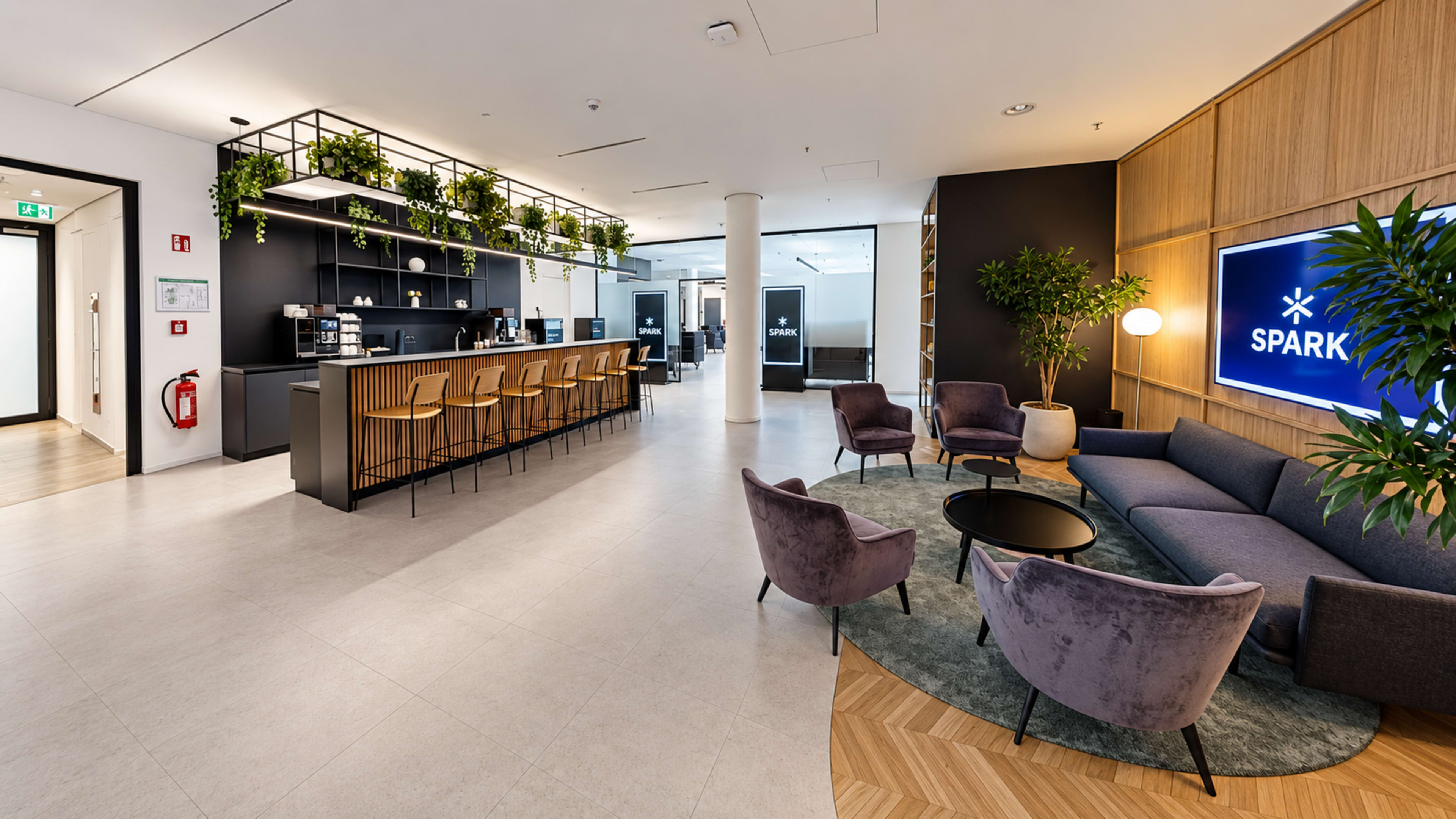 The image shows a modern reception area with a bar-style counter, seating arrangements, and various indoor plants, creating a welcoming atmosphere.