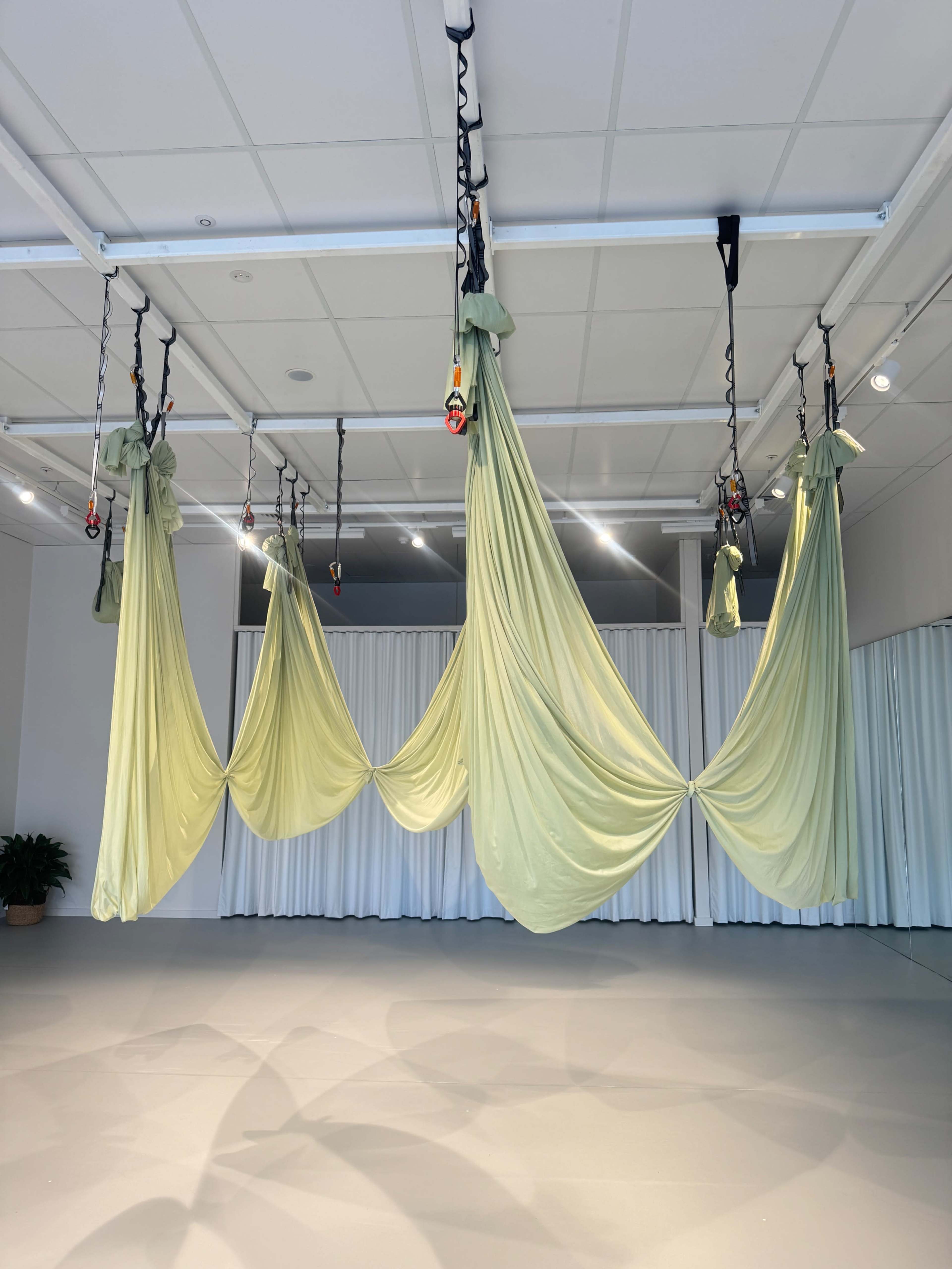 The image shows a spacious studio with three green draped fabric pieces suspended from the ceiling, creating a flowing arrangement.