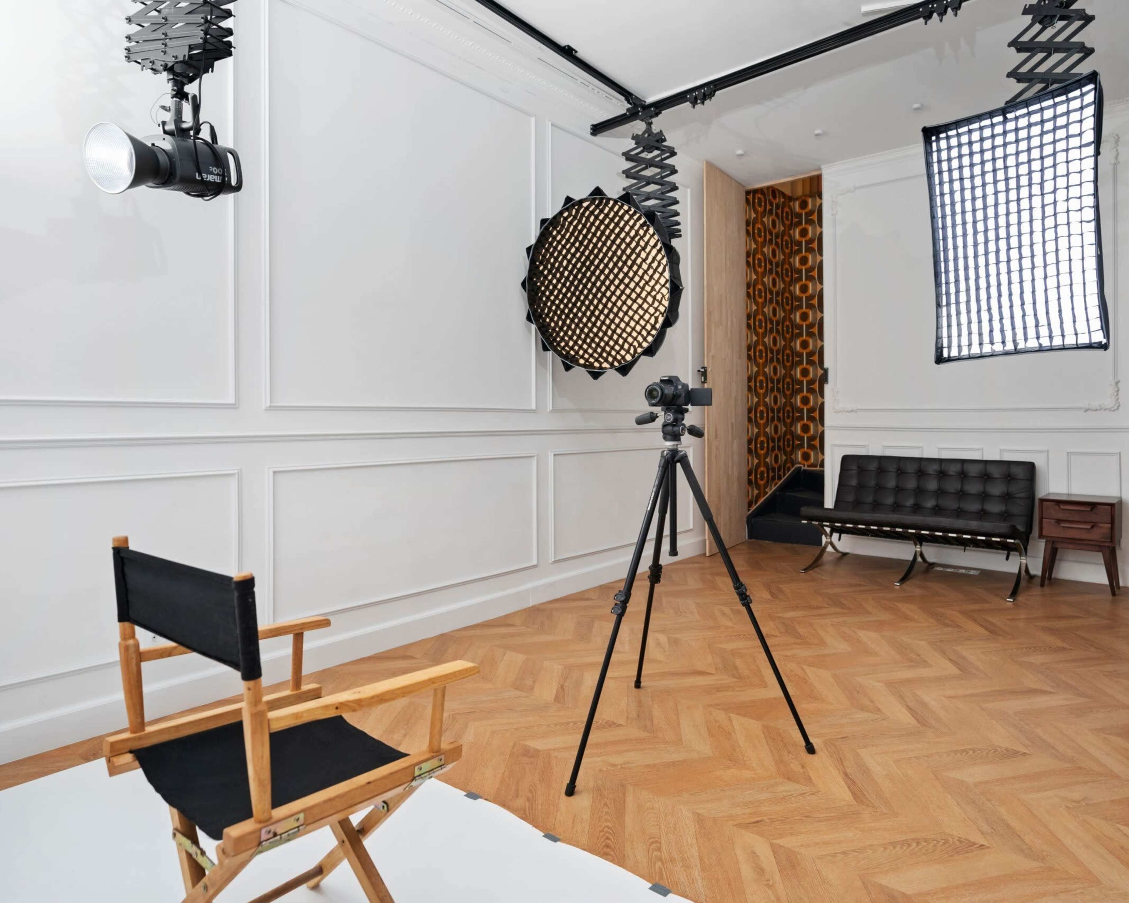 The image shows a photography studio featuring a director's chair, a camera on a tripod, and various lighting equipment.