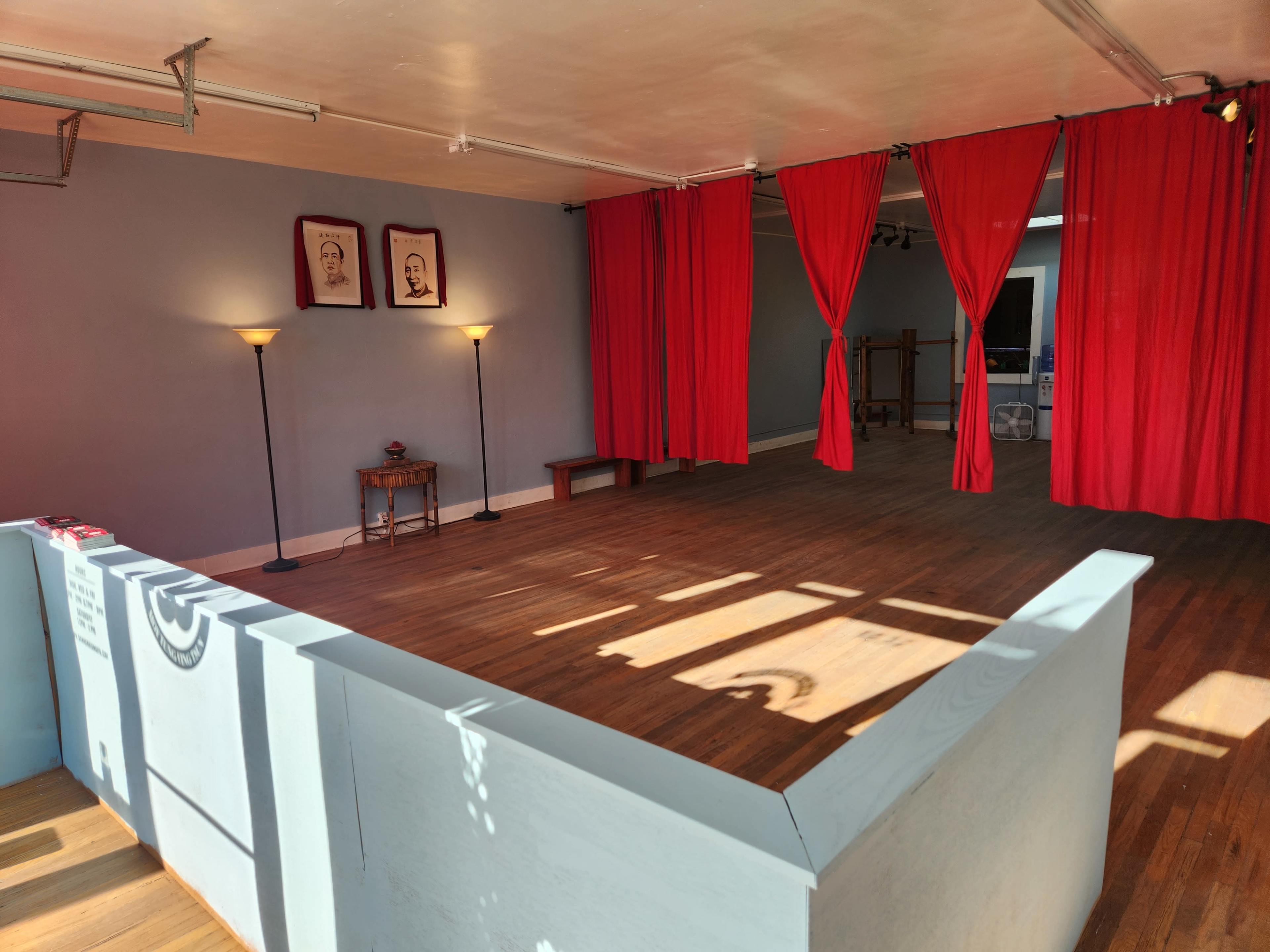 The image shows a spacious room with wooden flooring, two lamps on either side, and red curtains partially drawn against a blue wall.