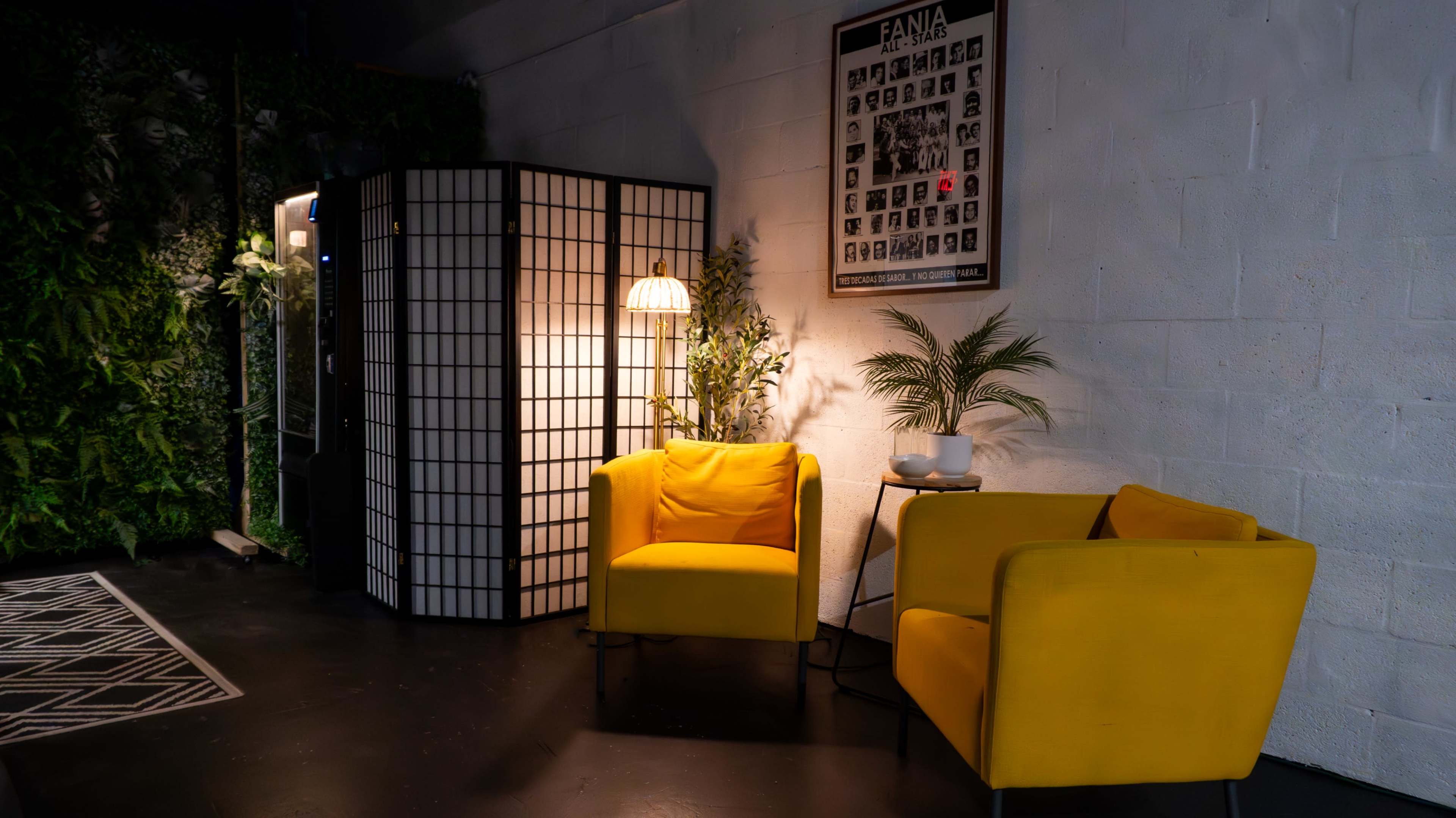 A cozy seating area features two yellow chairs beside a floor lamp, against a backdrop of green plants and a decorative screen.