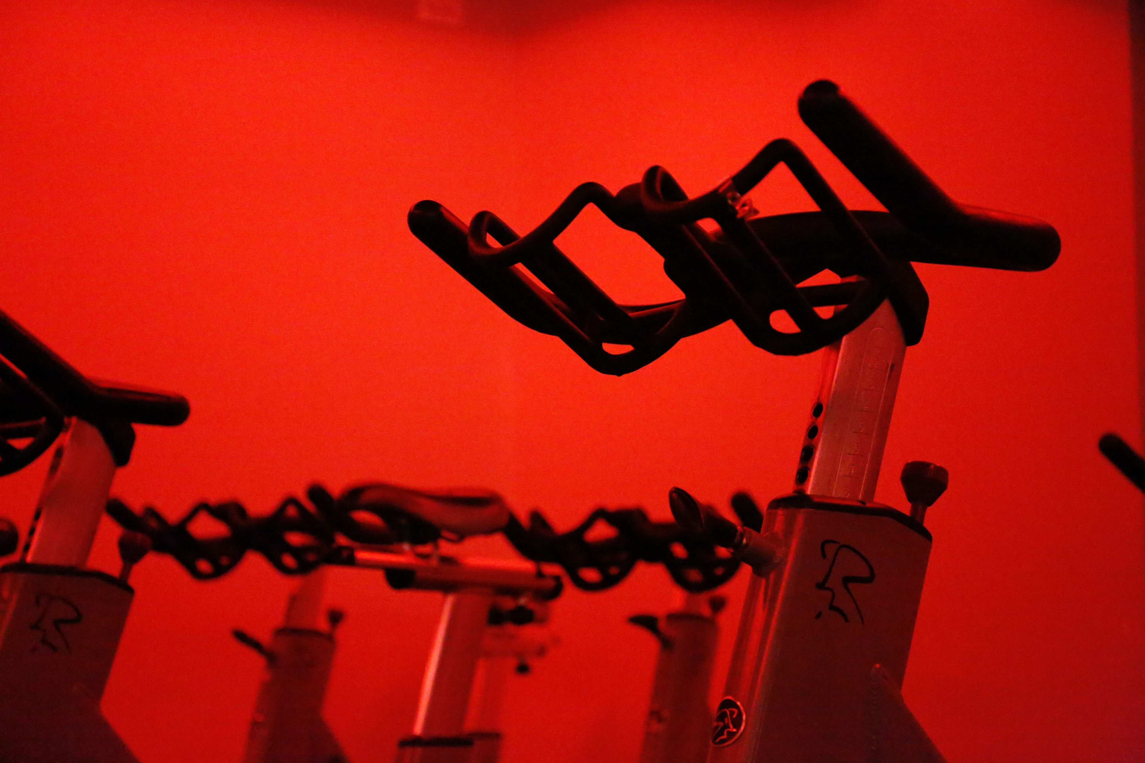 A row of stationary bicycles is illuminated by red light in a dimly lit room.