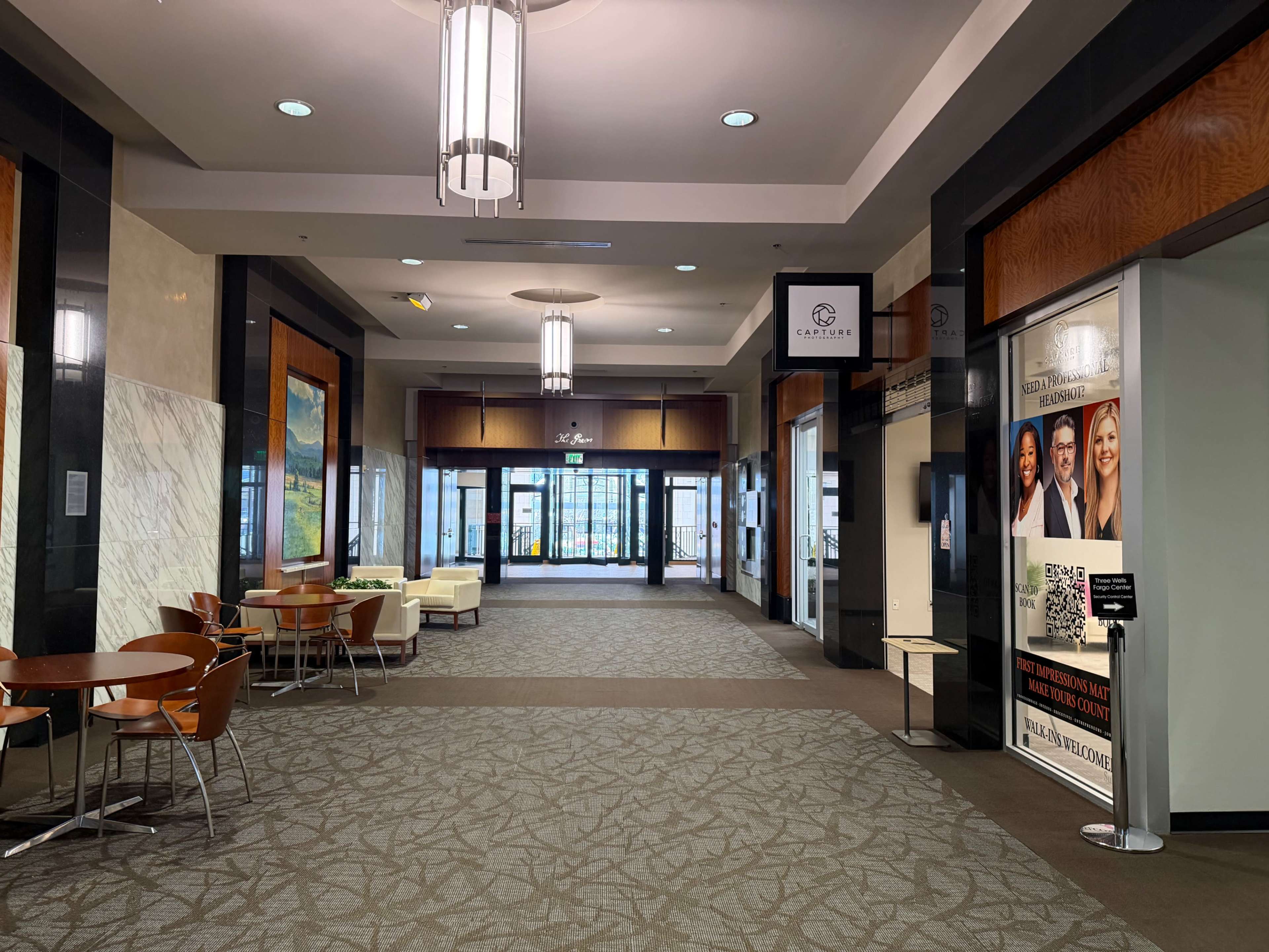 The image shows the interior of a modern building lobby with seating areas and glass entrance doors.