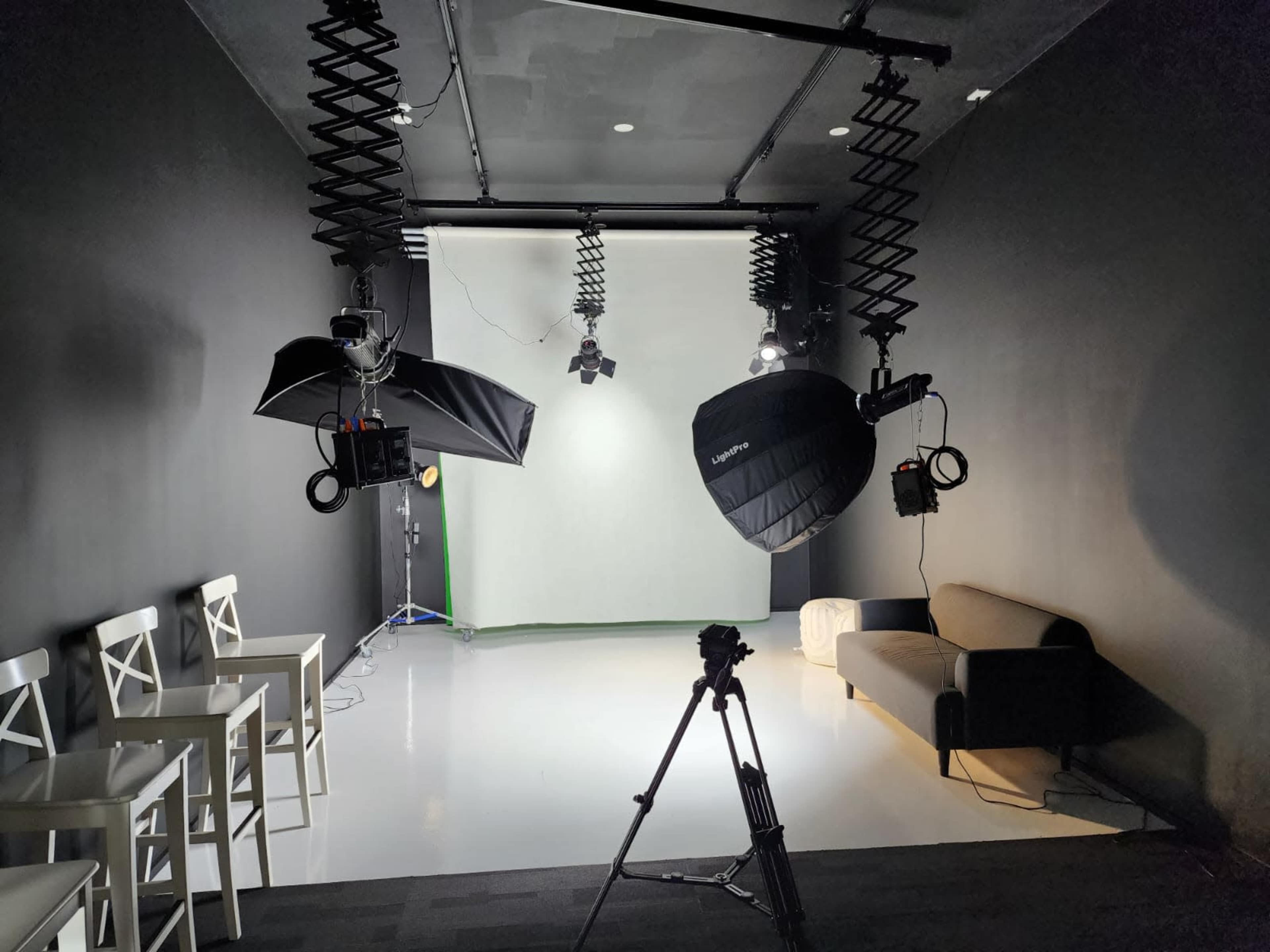 A photography studio with equipment including lights, a camera tripod, and a sofa against a black wall.