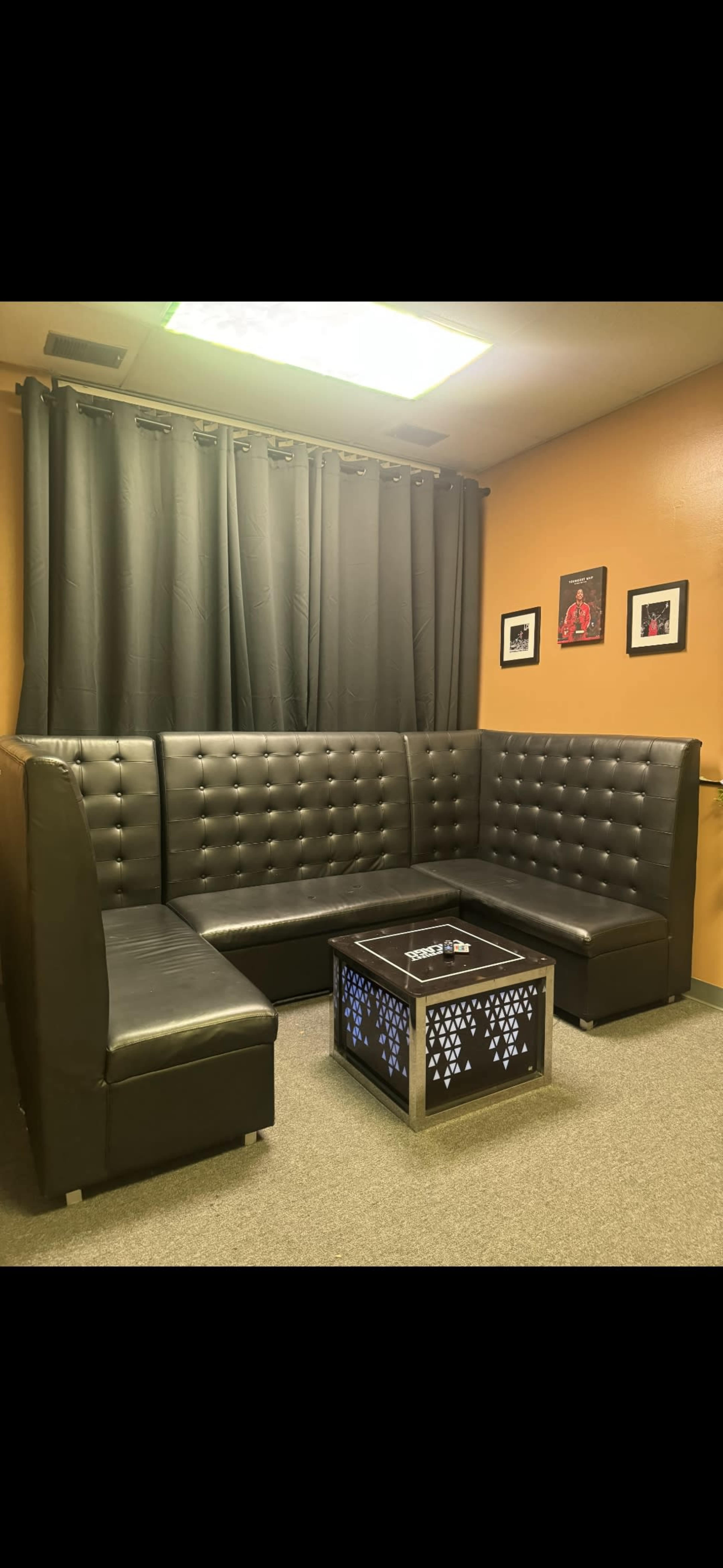 The image shows a modern seating area with a large black upholstered sectional couch and a decorative coffee table, situated against a warm orange wall.