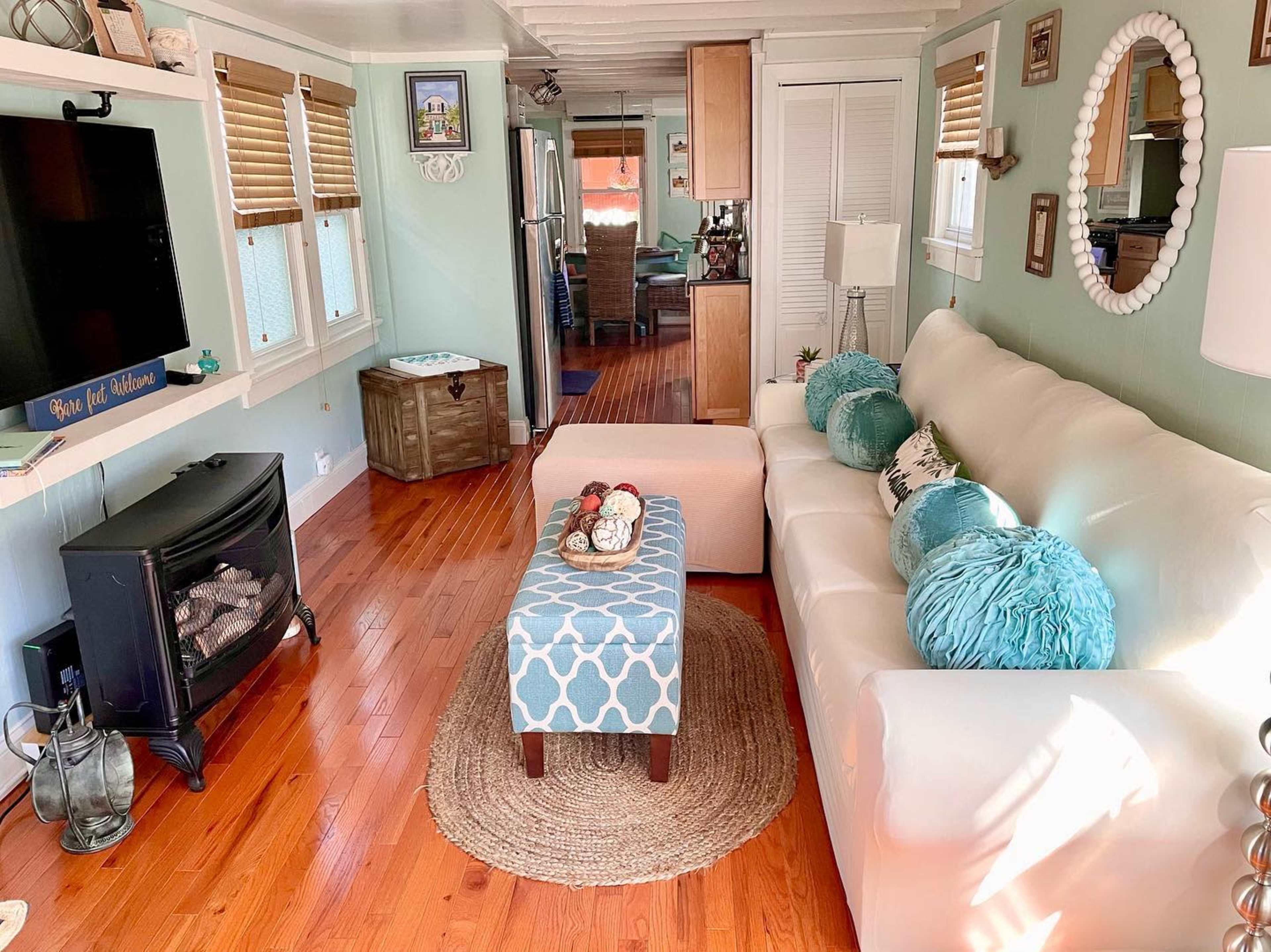 The living room features a white couch, a blue-patterned ottoman, and a fireplace, with wood flooring and green walls.