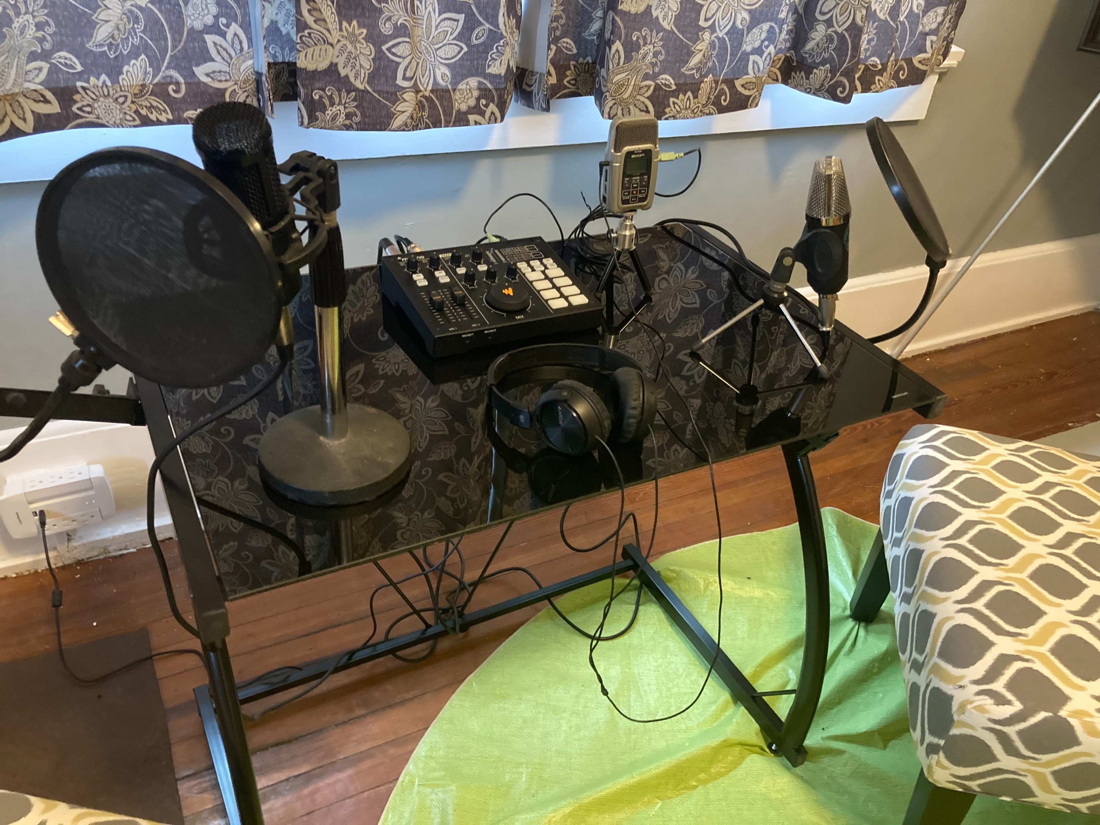 A black glass desk holds various audio equipment, including microphones, headphones, and a mixer, with tangled cables surrounding the setup.