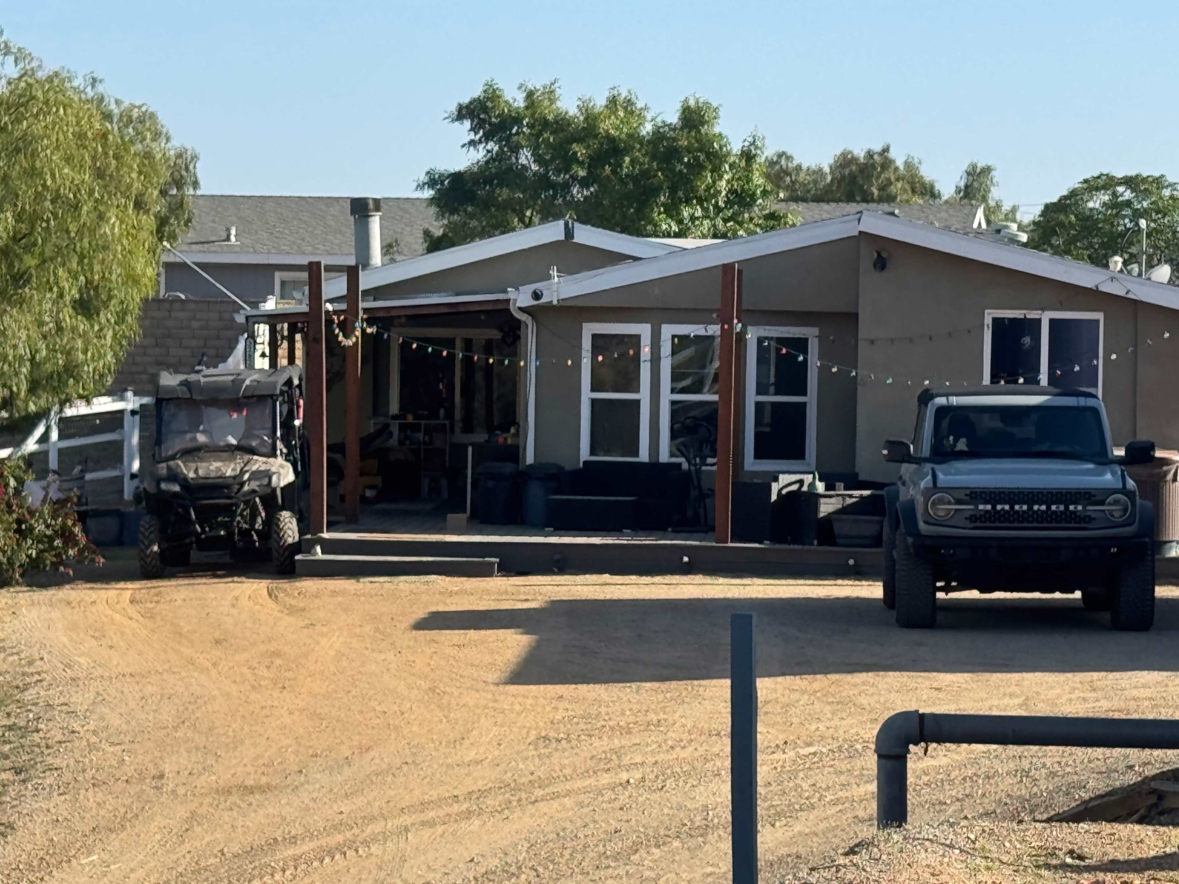 The image shows a house with a front porch, a parked pickup truck, and a utility vehicle in a dirt driveway surrounded by trees.