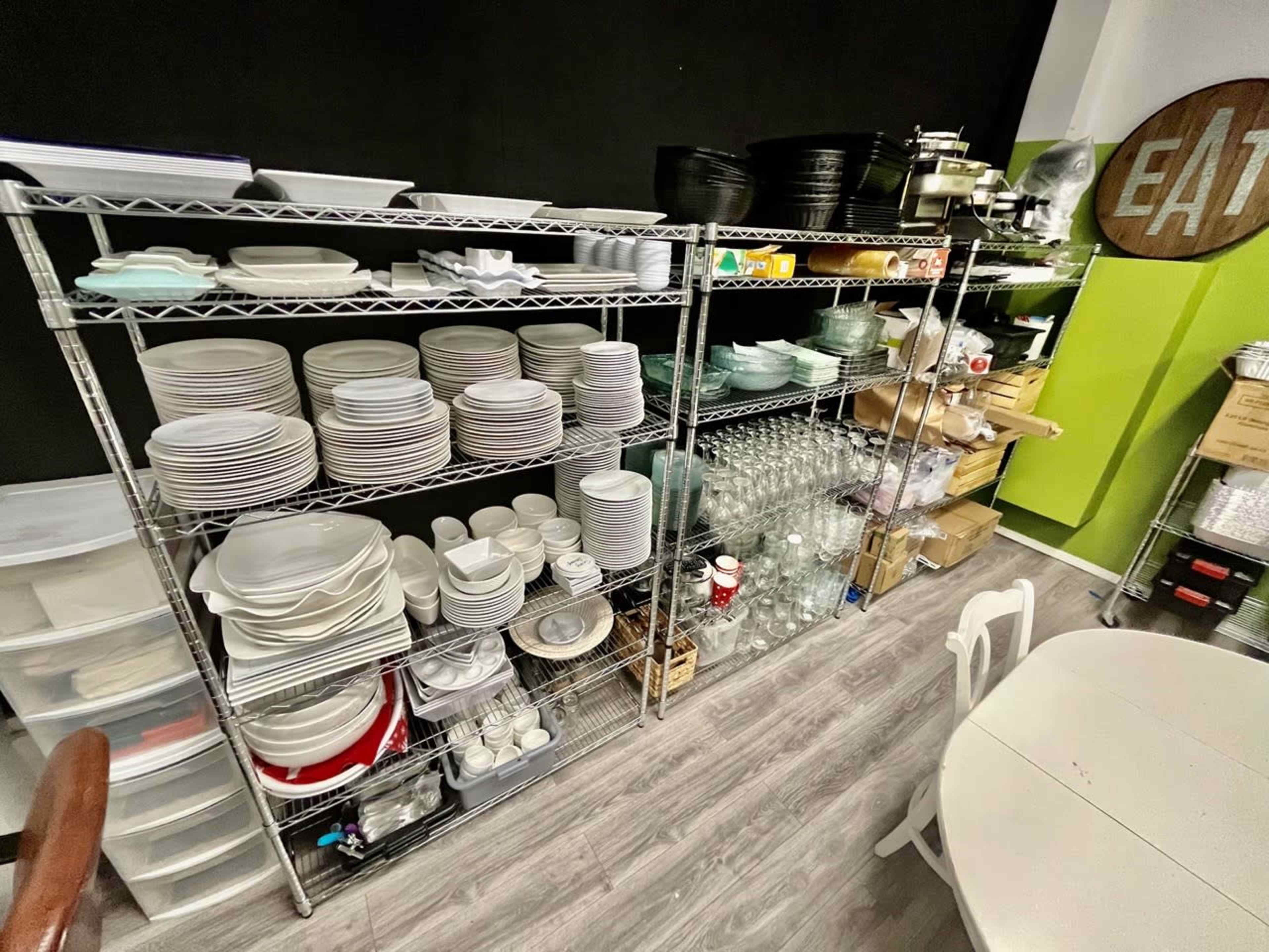 Metal shelving units filled with various dishes, glassware, and kitchen supplies in a well-organized storage area.