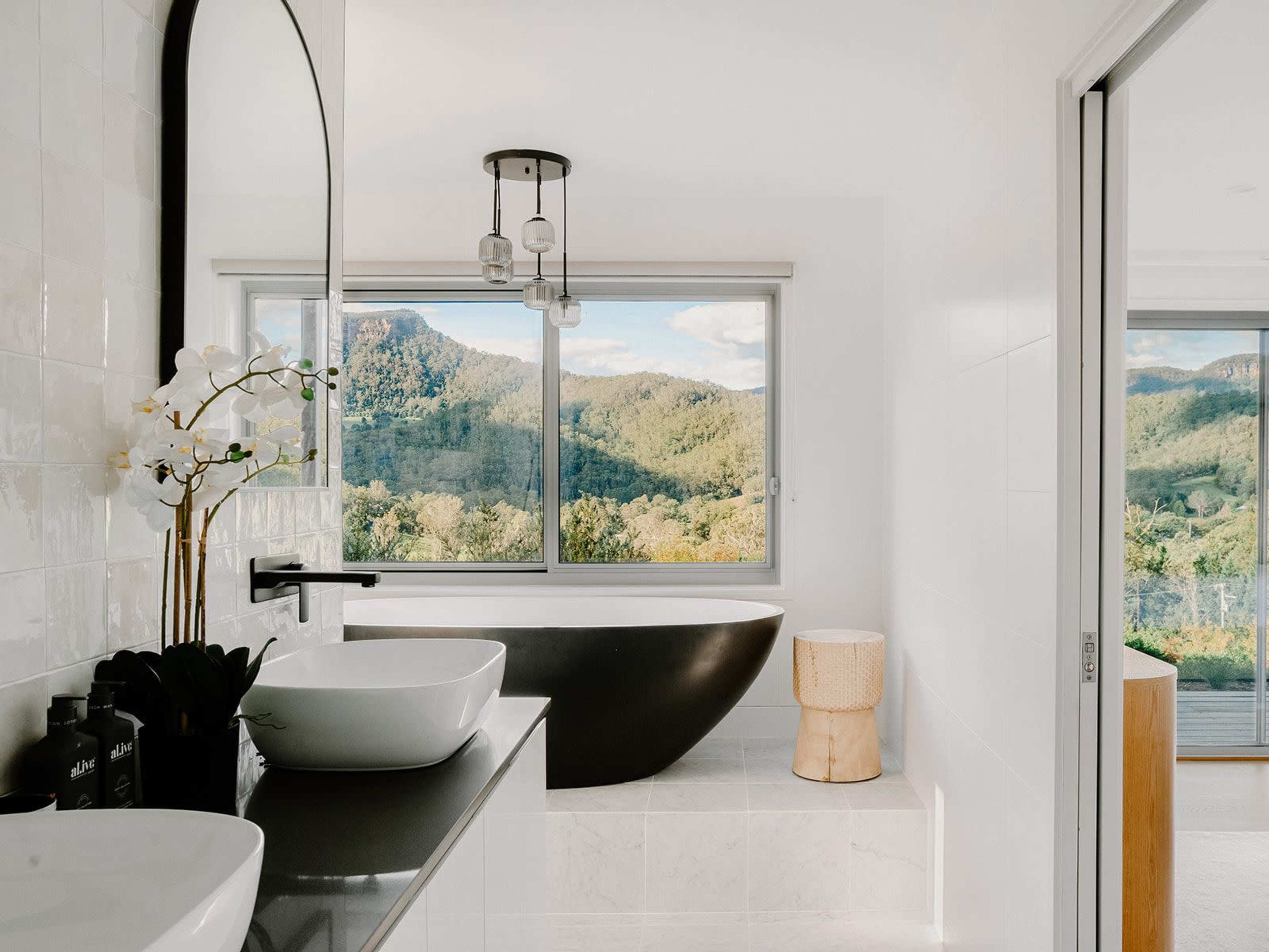 A modern bathroom featuring a freestanding black bathtub next to large windows that offer a view of mountains outside.