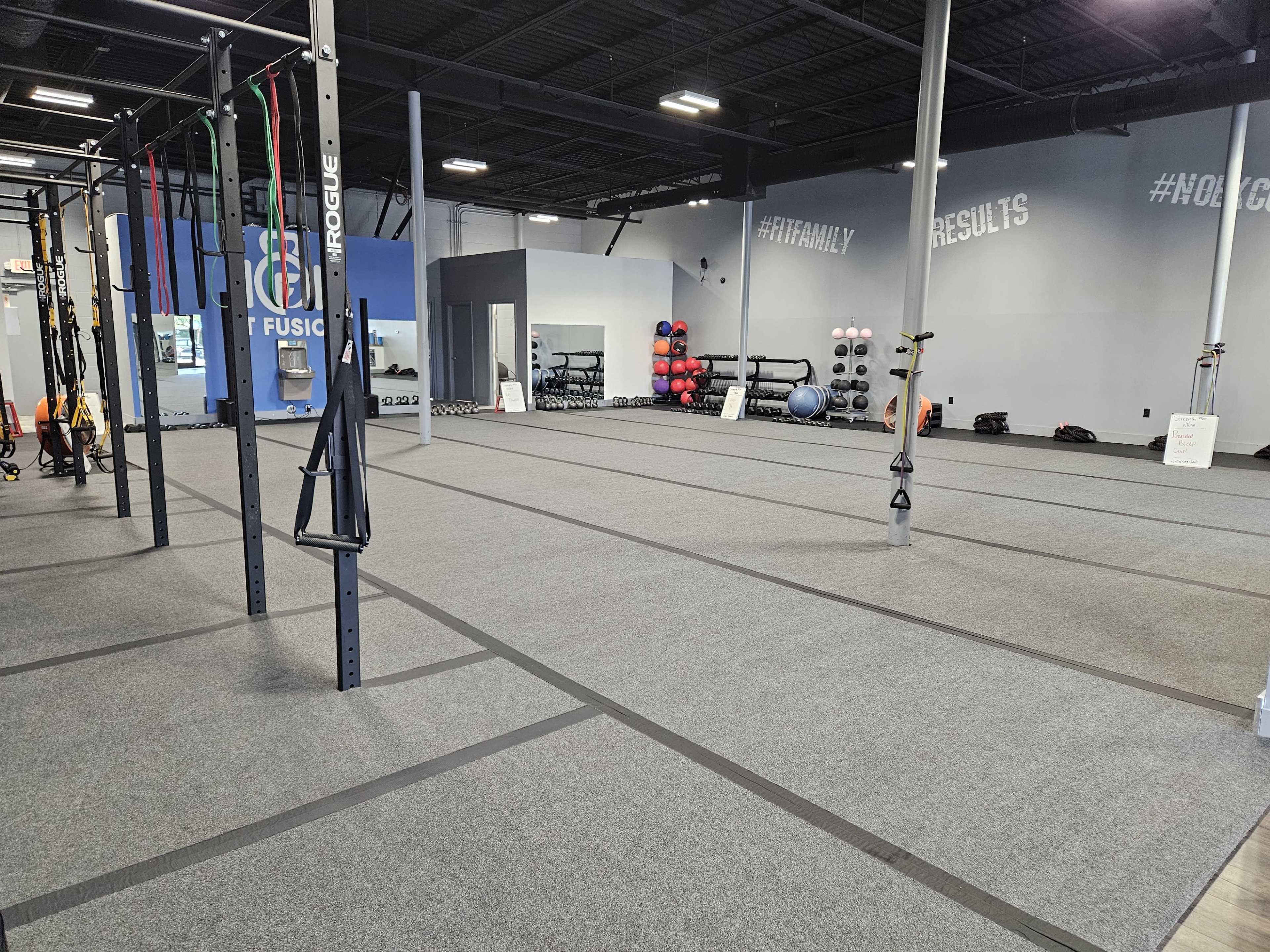 A spacious gym interior with exercise equipment, including suspension trainers and a variety of weighted balls, on neatly arranged rubber flooring.
