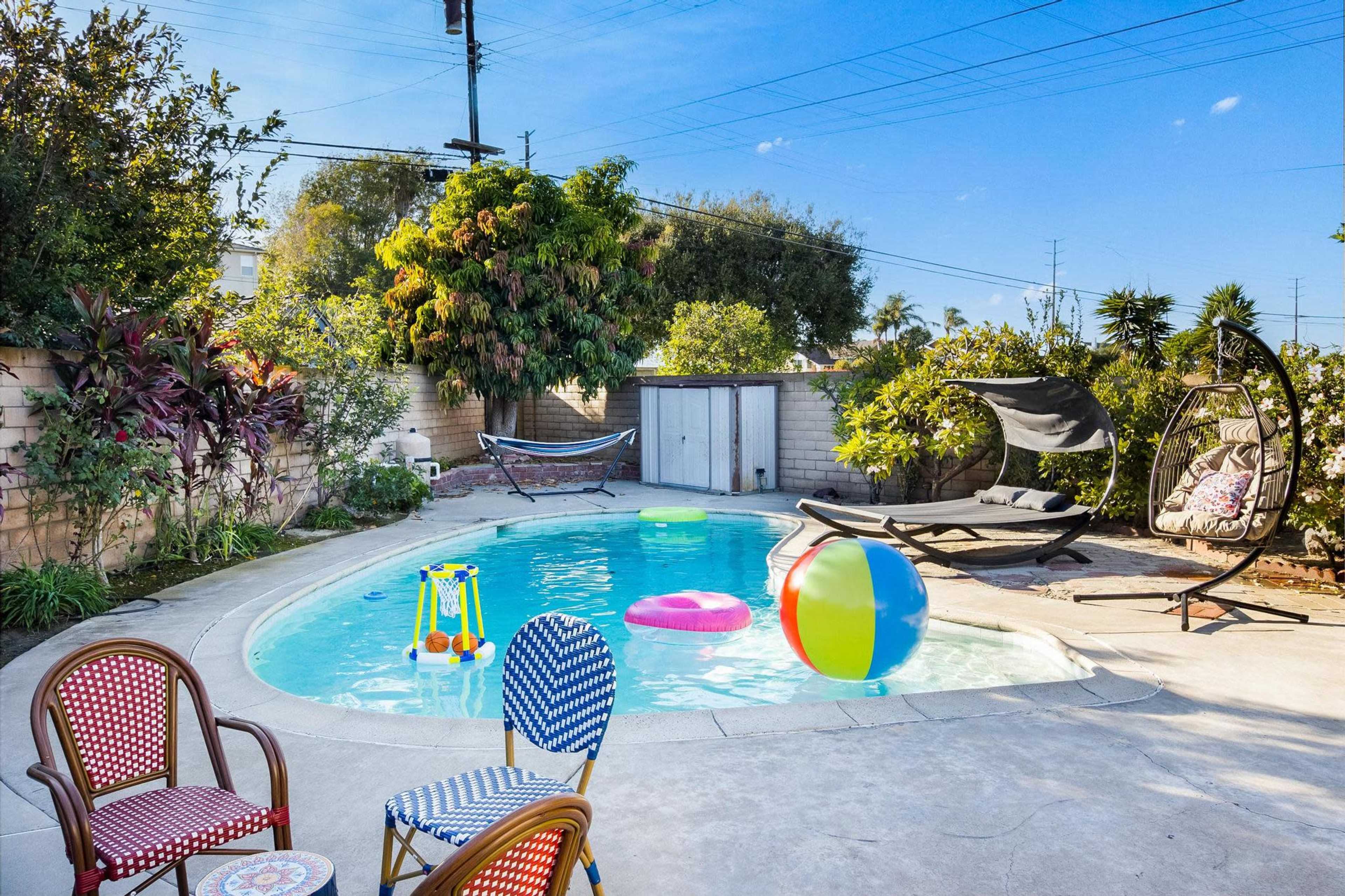 A backyard pool surrounded by colorful inflatable toys, a hanging chair, and outdoor seating.