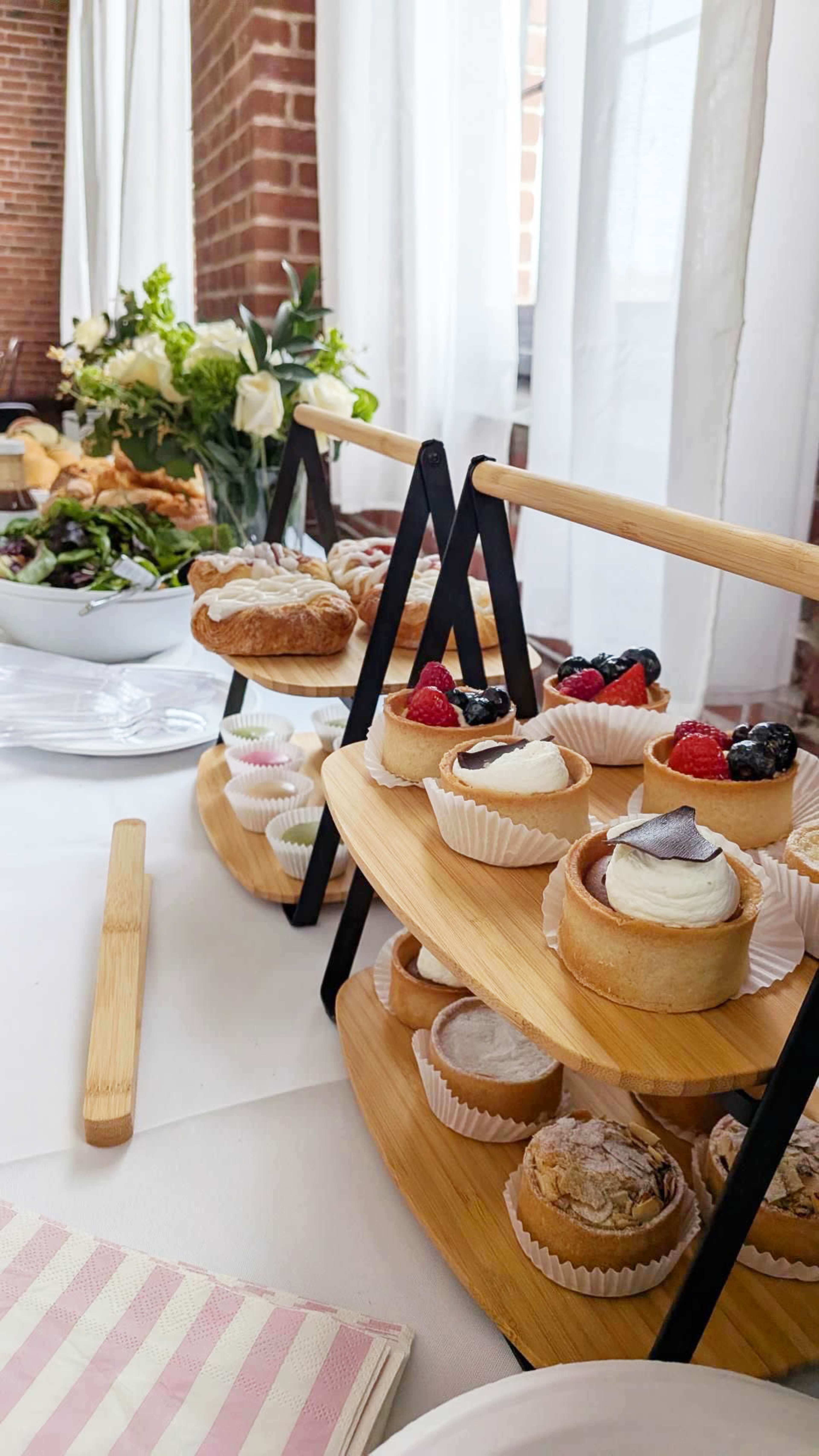The image displays a tiered stand filled with various pastries and desserts, complemented by a floral arrangement and a salad on a table.