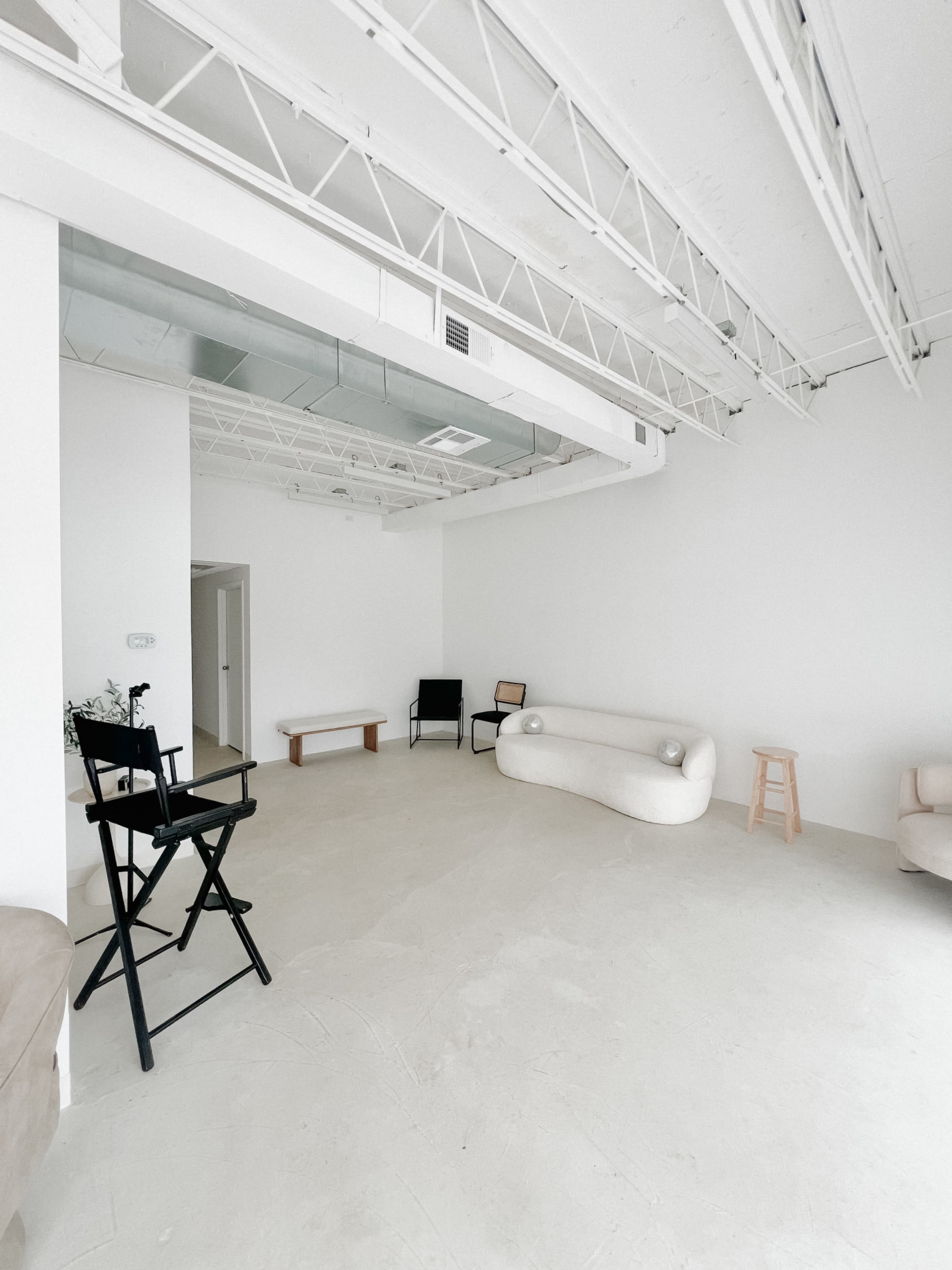 The image shows a minimalist room with a light-colored floor, white walls, and various seating arrangements, including curved and straight benches.