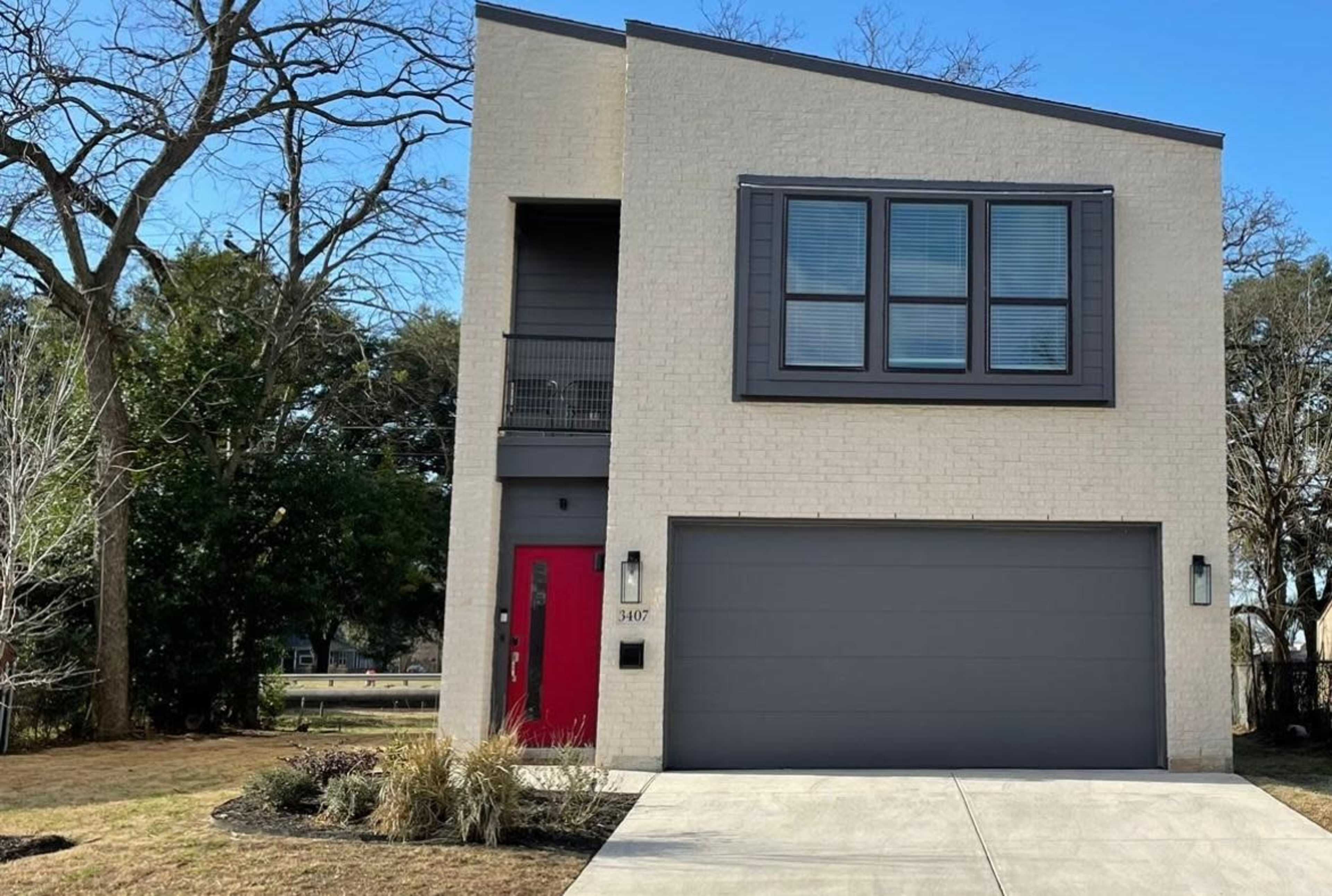 A modern two-story house with a red front door, large windows, and a gray garage, set in a landscaped yard.