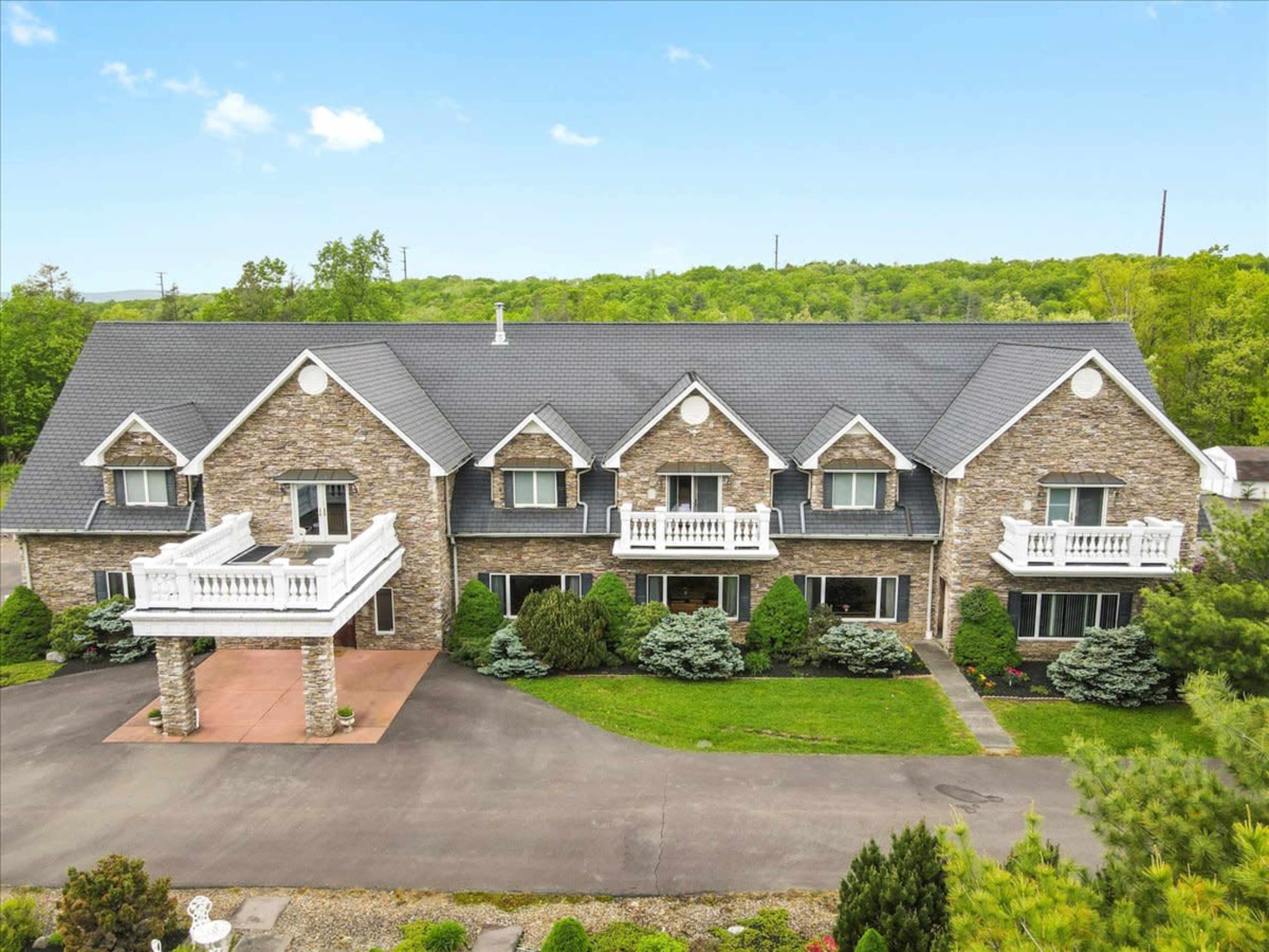 A large brick house with multiple balconies, set in a landscaped area surrounded by trees.