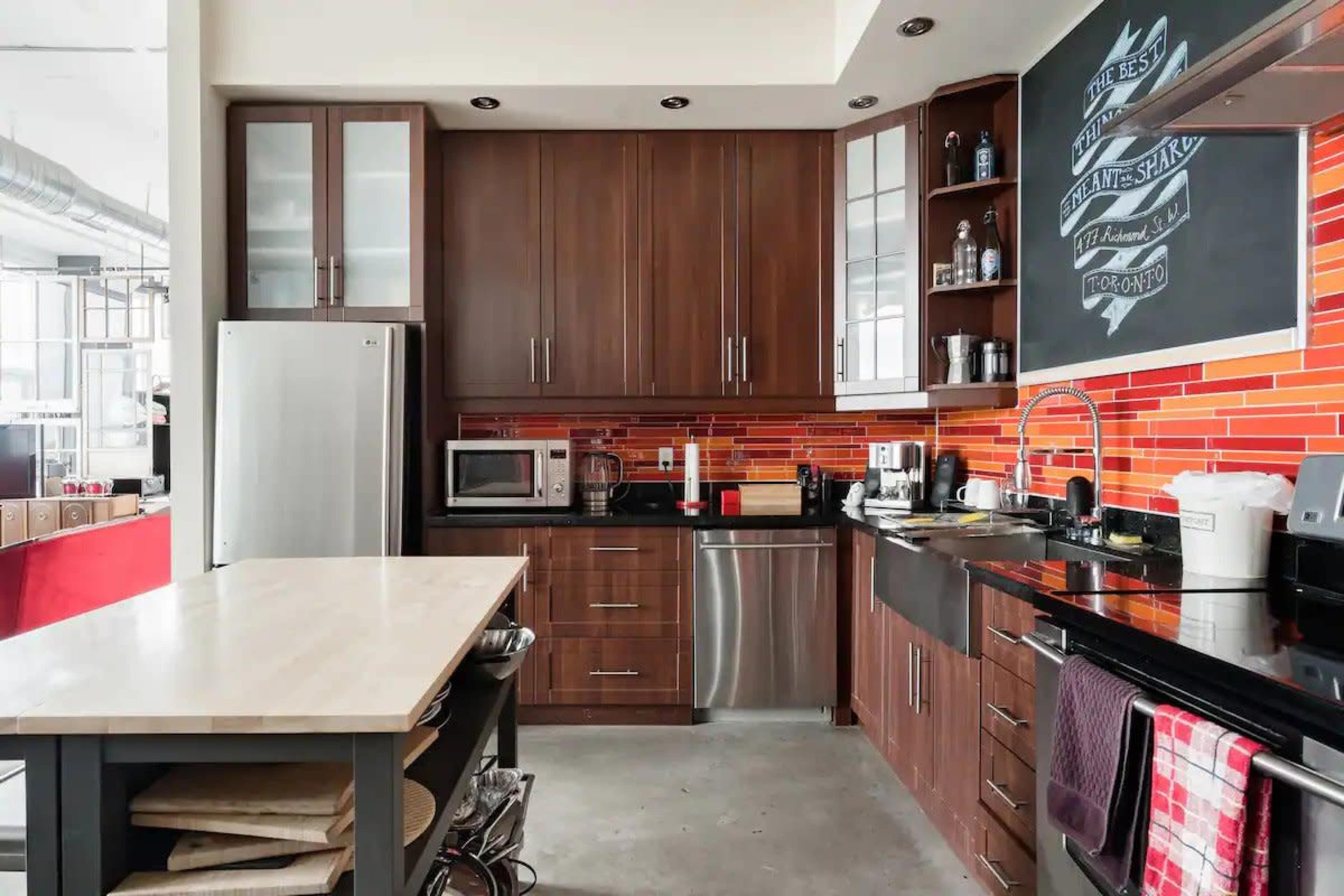 The kitchen features dark wood cabinets, a stainless steel refrigerator, black countertops, and a vibrant orange tile backsplash.