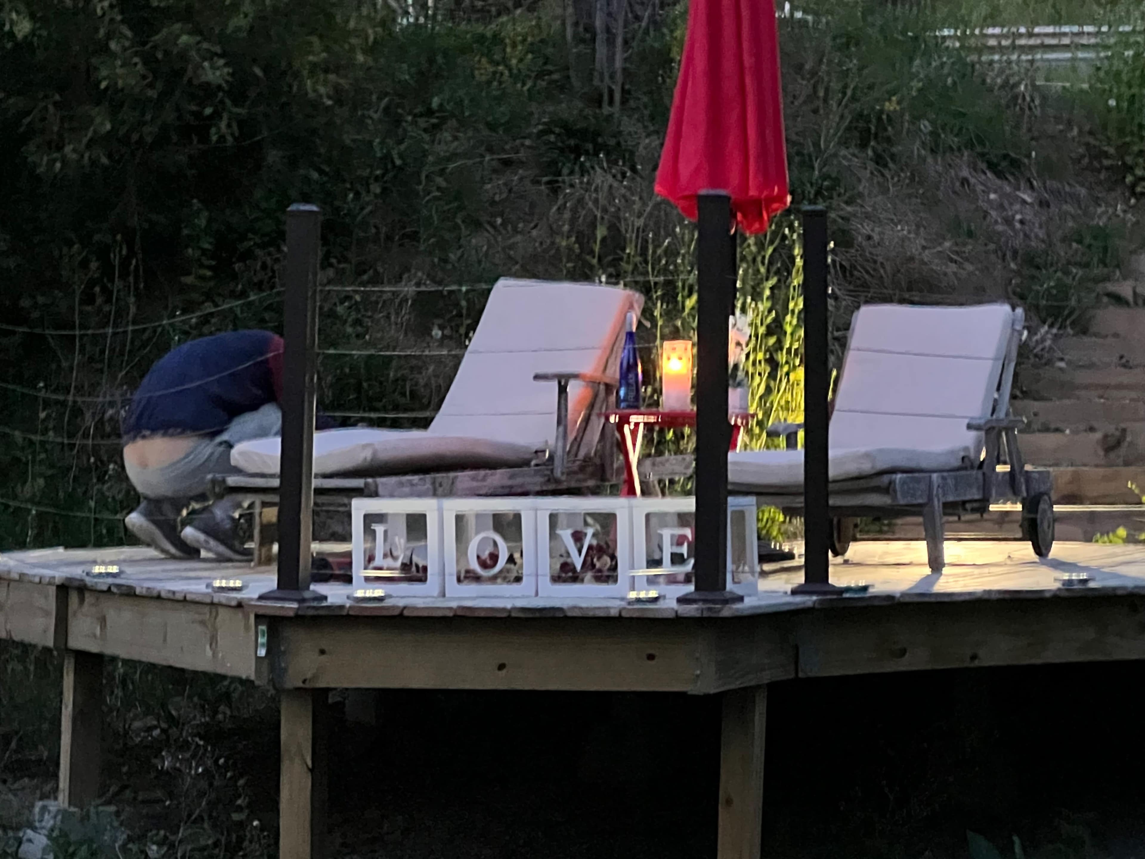 A person is adjusting a lounge chair on a wooden deck illuminated by a lamp and surrounded by decorative letters spelling "LOVE."