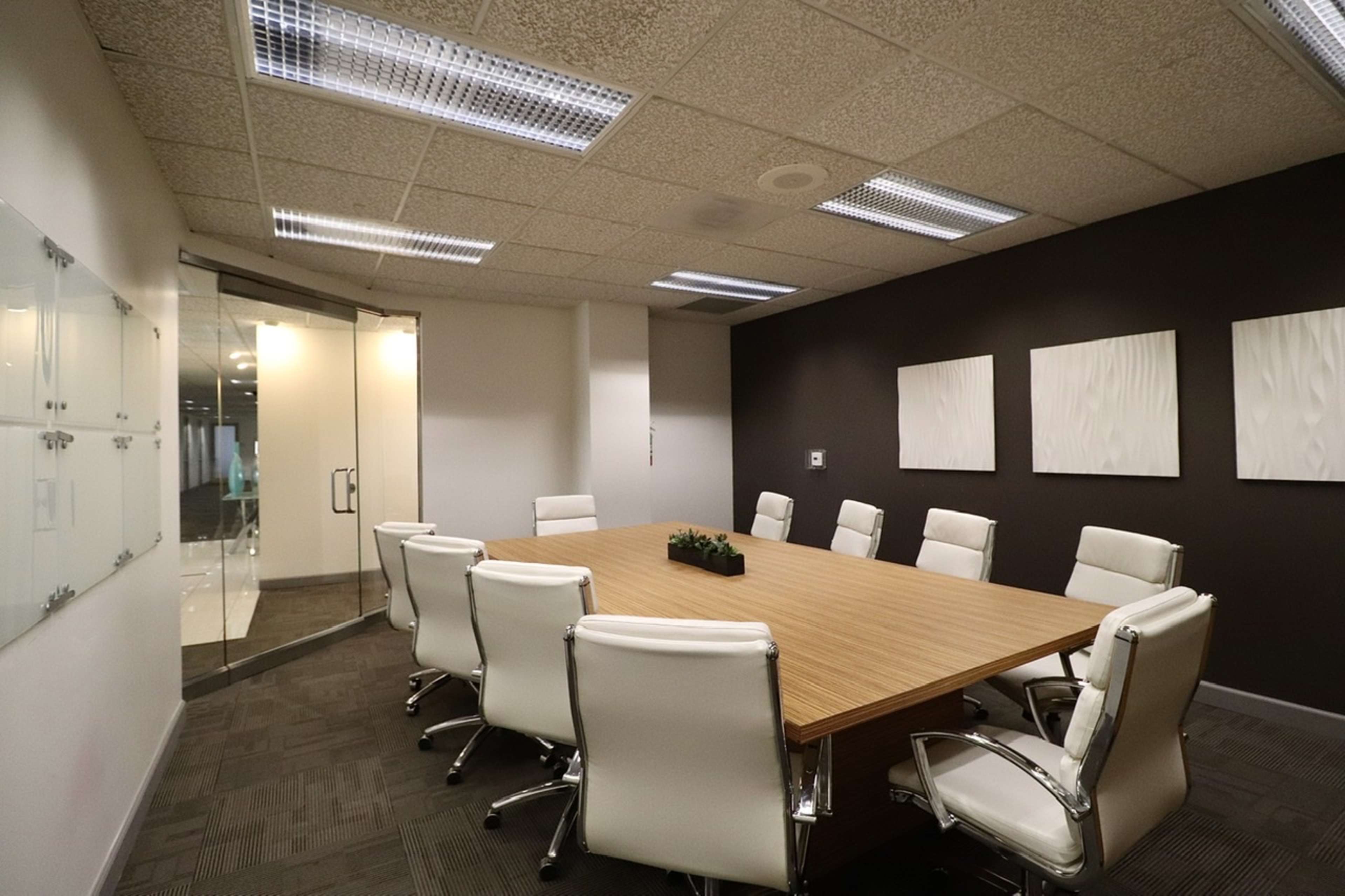 A conference room with a large wooden table surrounded by eight white leather chairs and modern wall art.