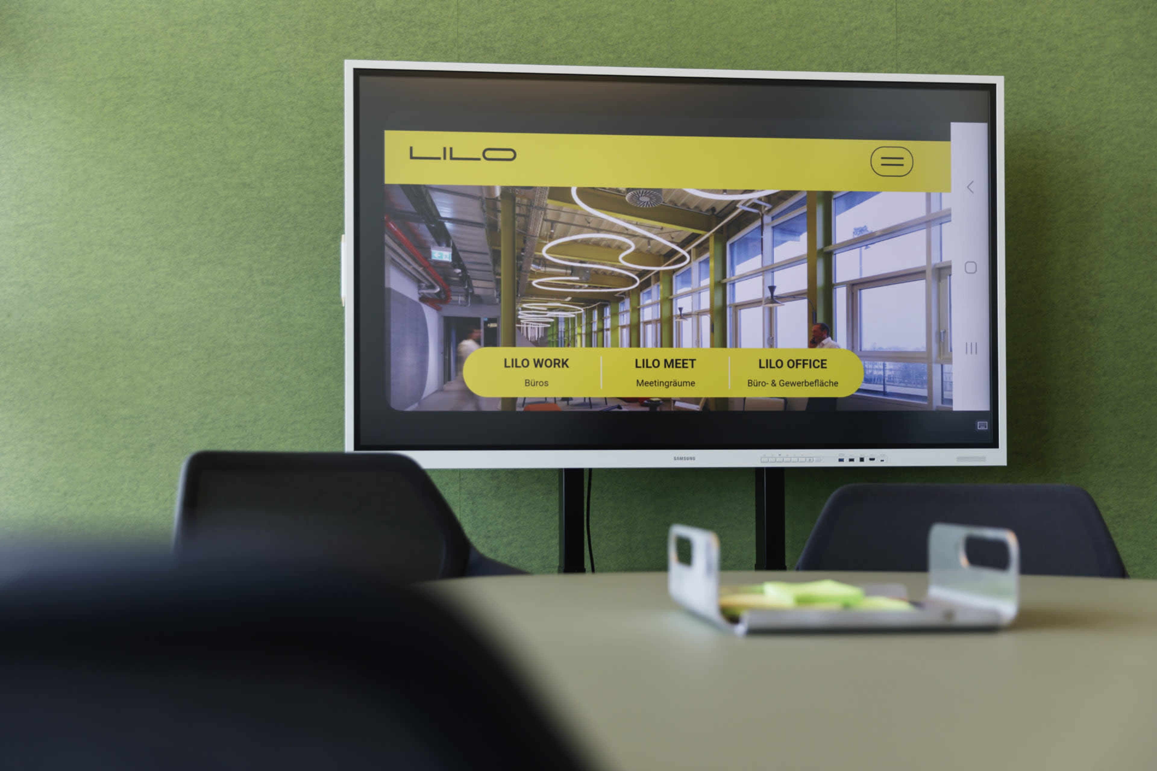 A digital display shows the LILO brand website with sections for "LILO Work," "LILO Meet," and "LILO Office" in a modern meeting room.