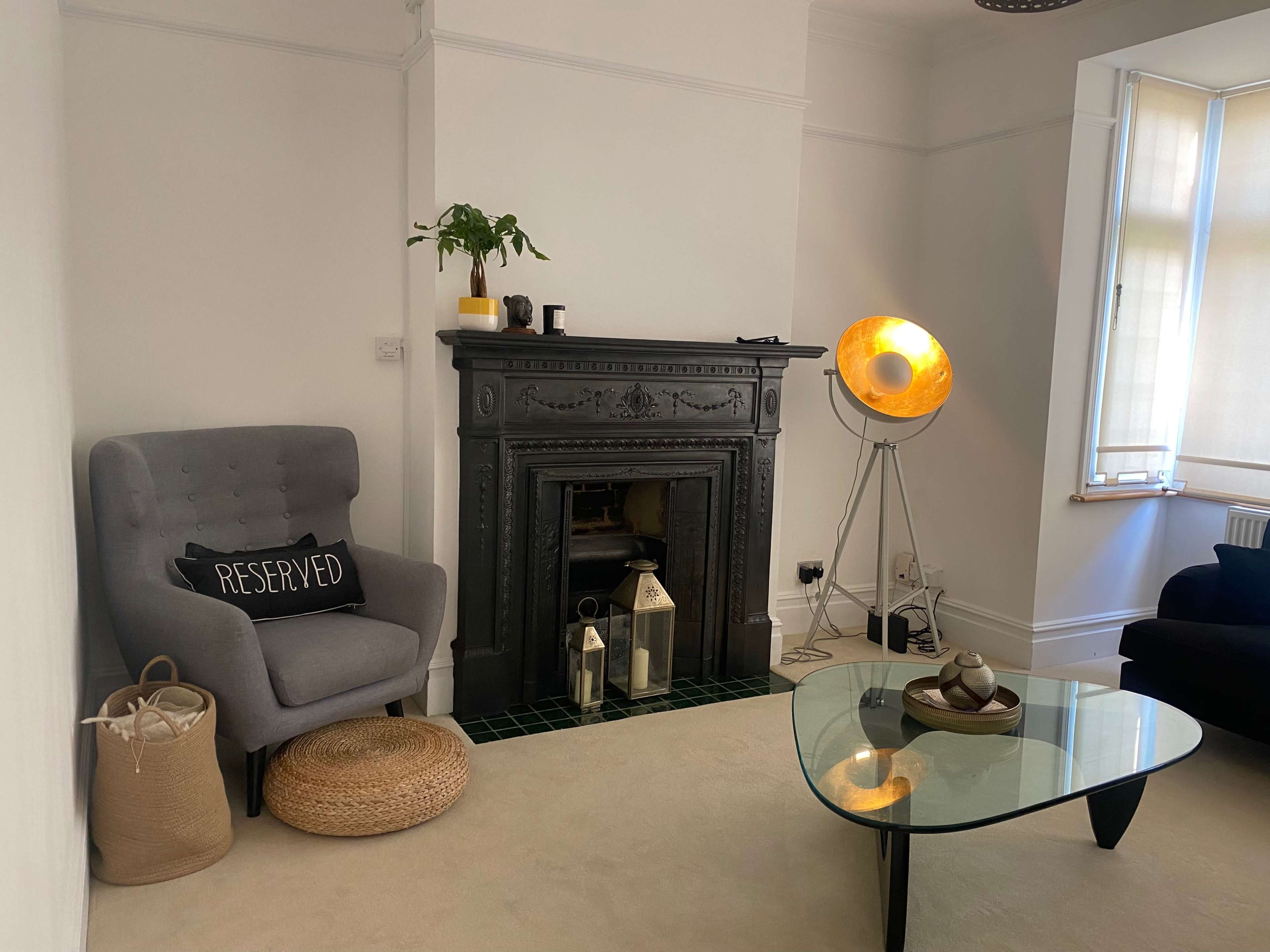 The image shows a living room with a gray upholstered chair, a decorative fireplace, a floor lamp, and a glass coffee table.