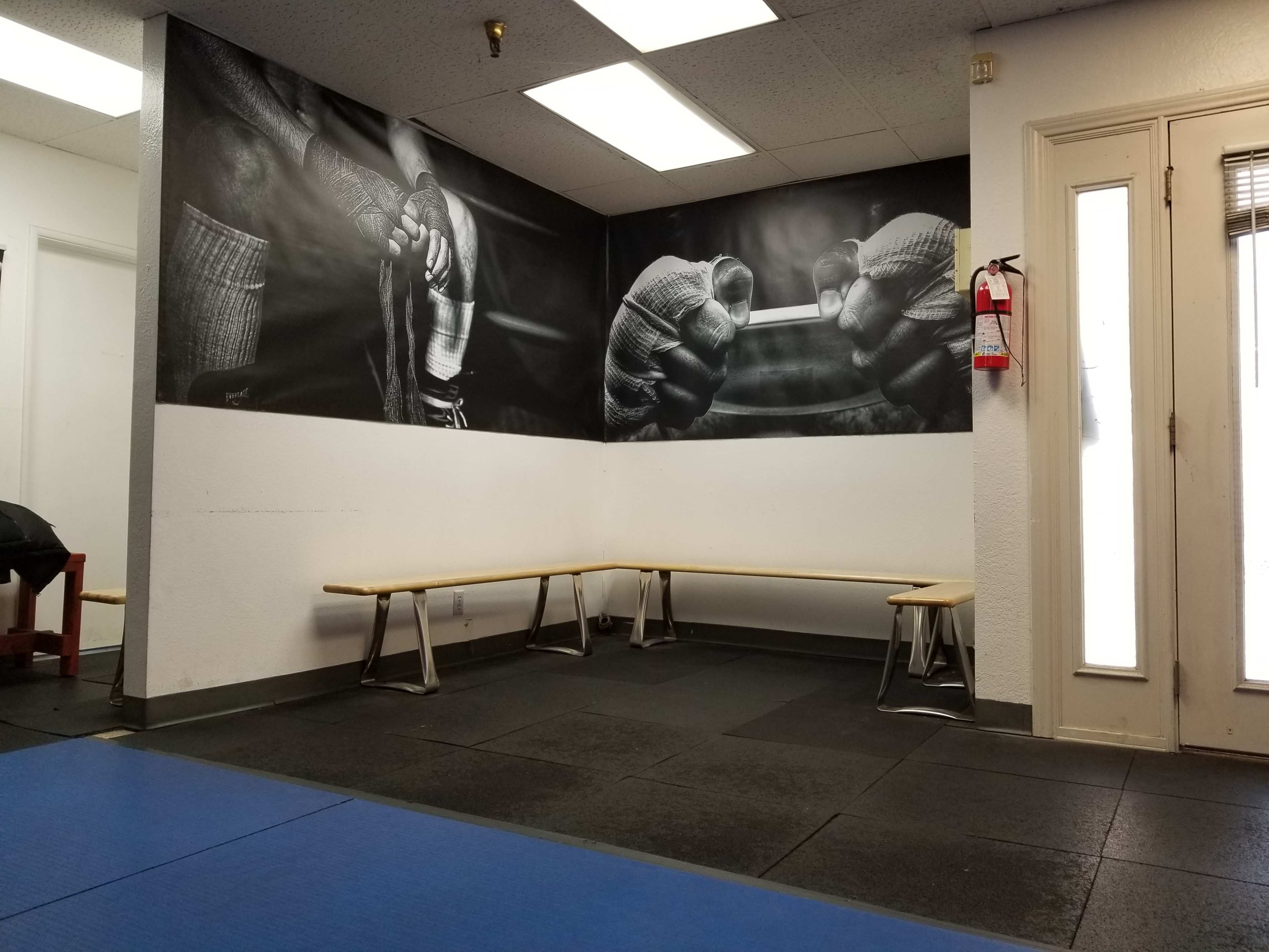 A training room with a large black and white mural of gloved hands preparing equipment, alongside a series of long benches against the walls.