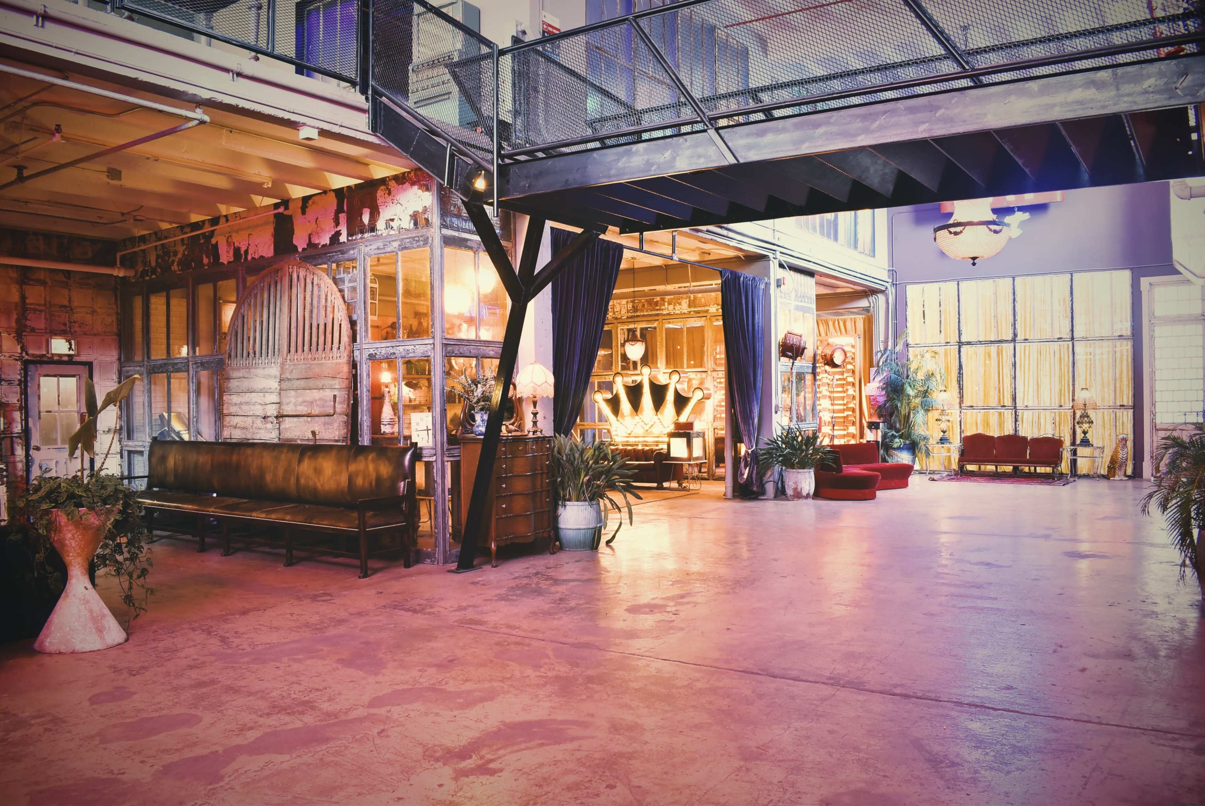 The image features a spacious industrial-style interior with a mix of seating areas, large windows, and decorative elements.