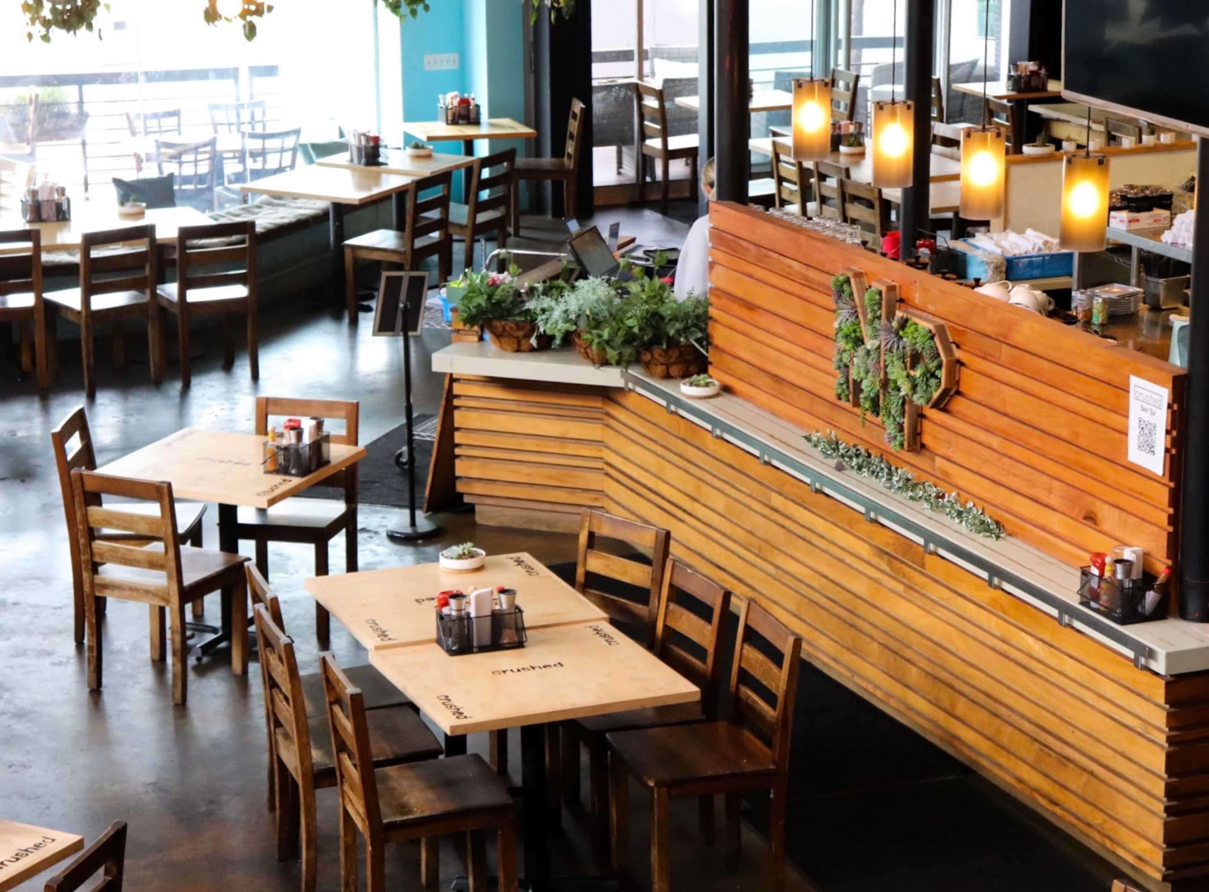 A spacious restaurant interior features wooden tables and chairs, with a counter displaying plants and QR codes.