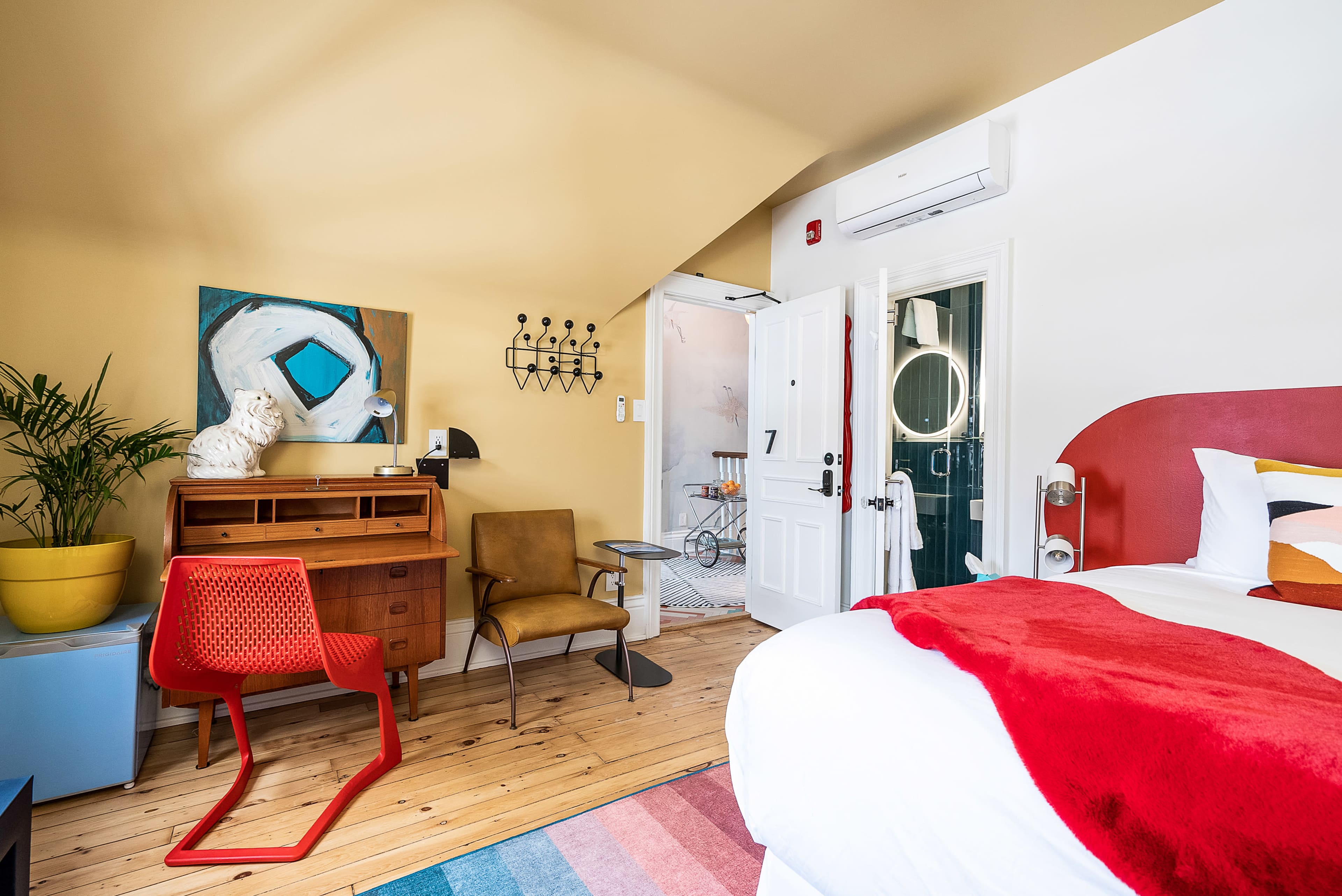 A brightly lit bedroom featuring a red accent wall, wooden flooring, and a mix of vintage and modern furnishings.