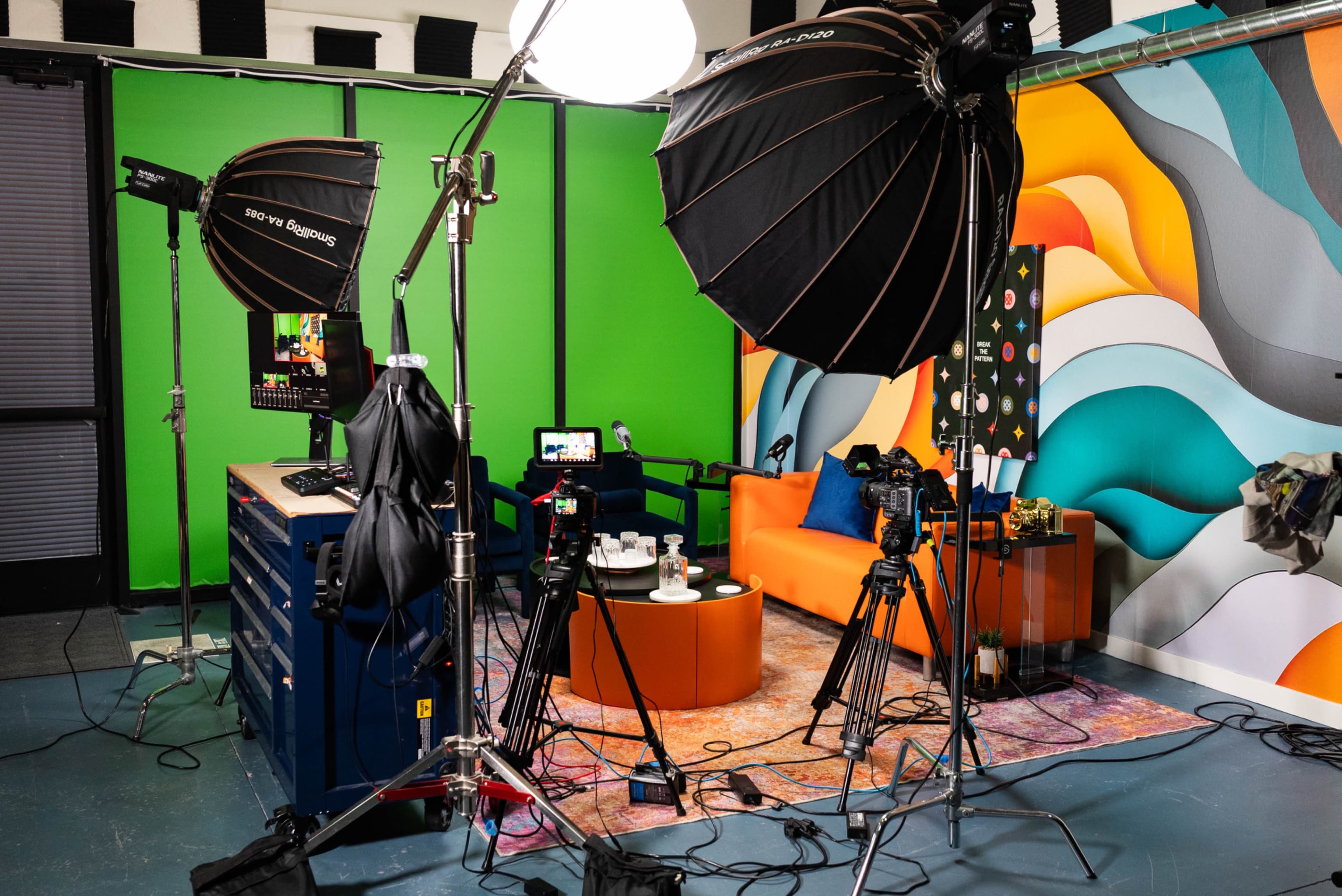 The image shows a photography studio setup with multiple cameras, lighting equipment, and a vibrant backdrop featuring abstract patterns.