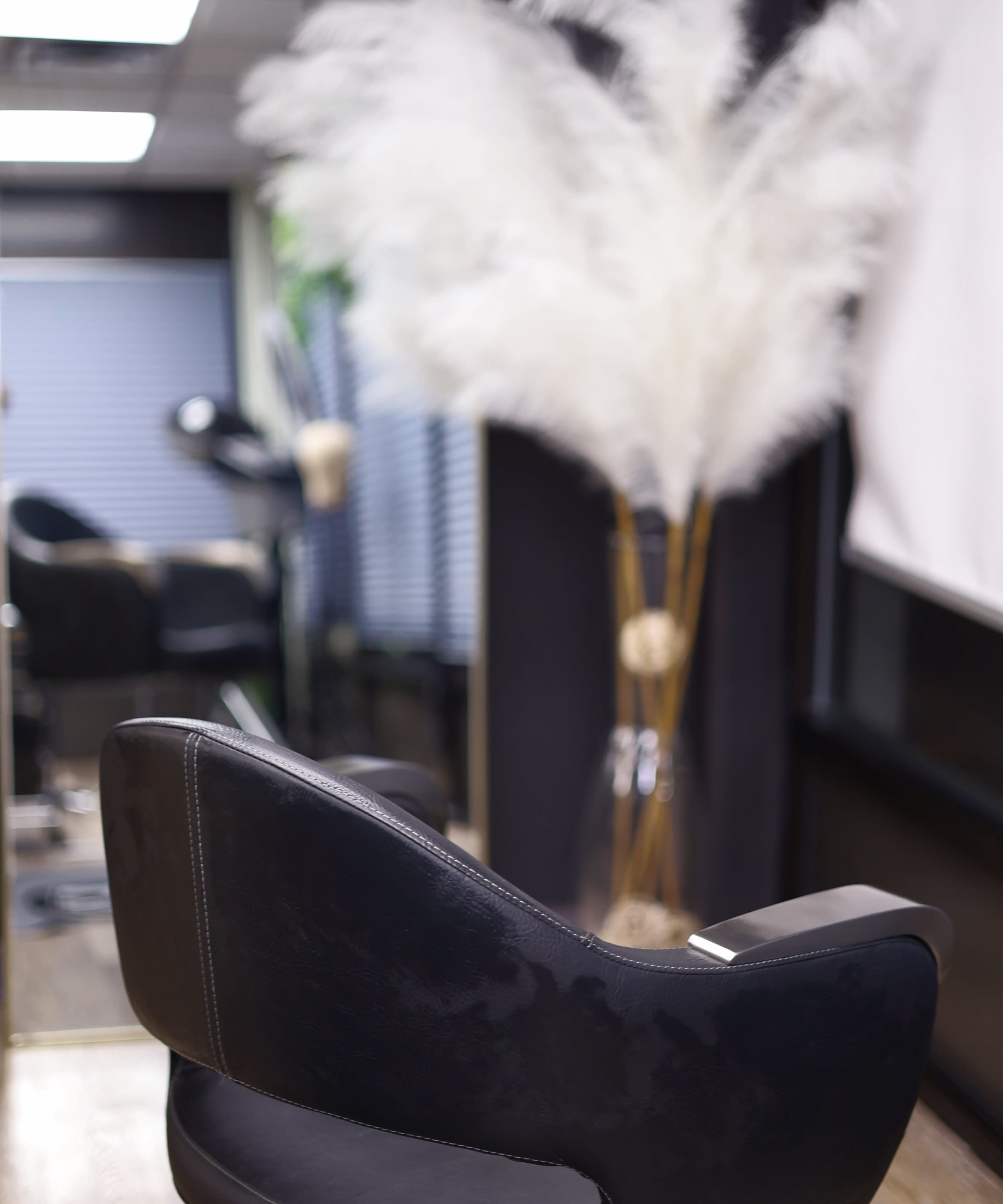 A black salon chair in front of a decorative arrangement of tall, white pampas grass.