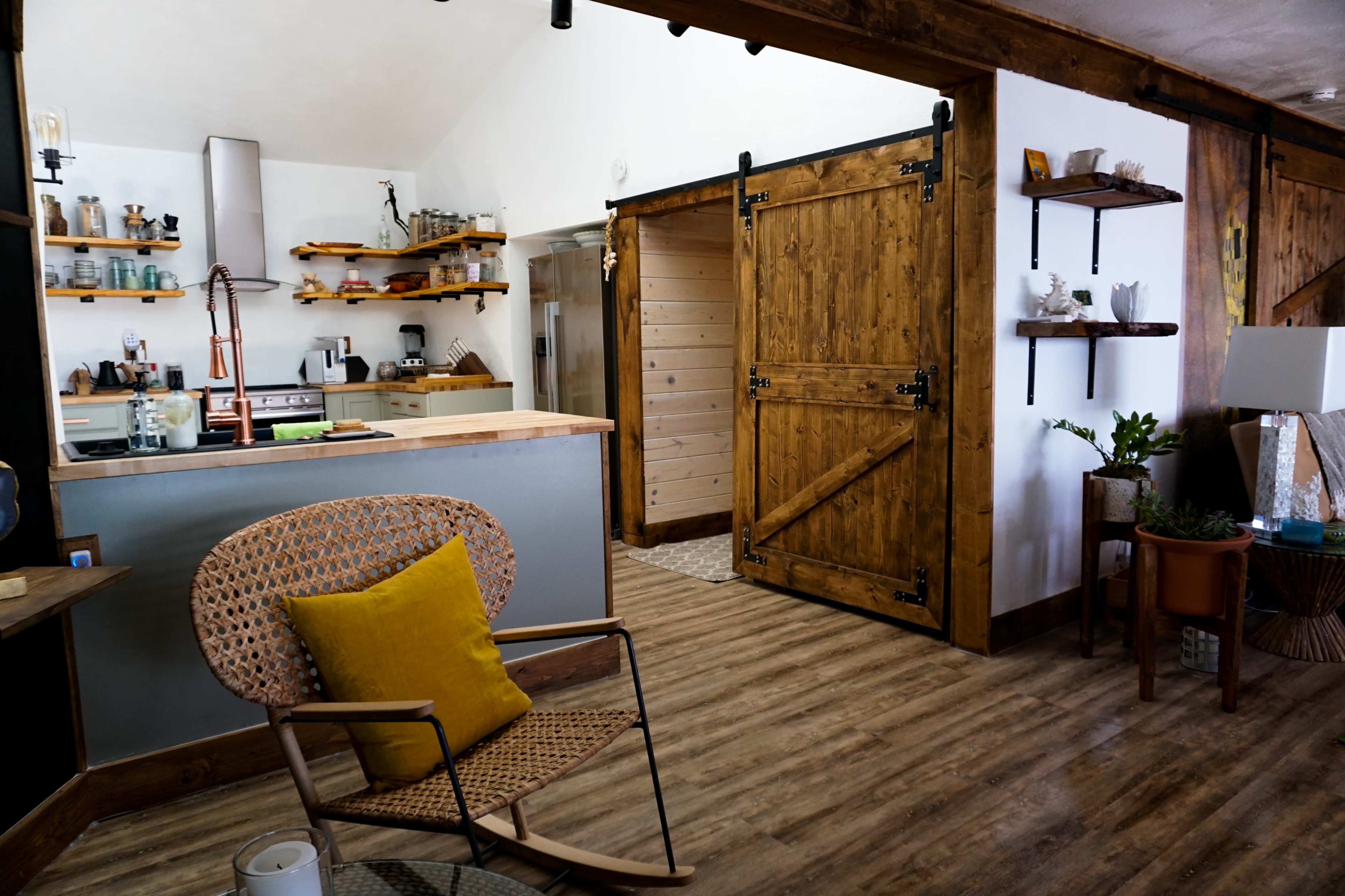 A modern kitchen area features wooden accents and a sliding barn door, with a woven chair and yellow cushion in the foreground.